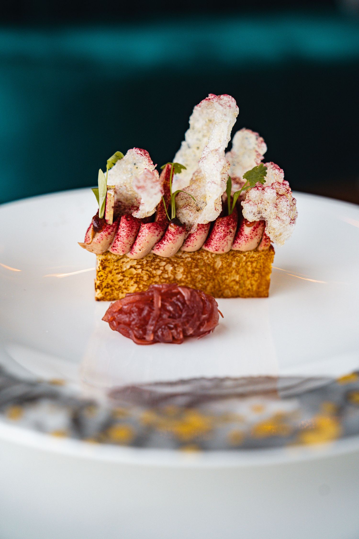 Artistic plating of a deconstructed dessert featuring pink meringue and red elements on white porcelain.