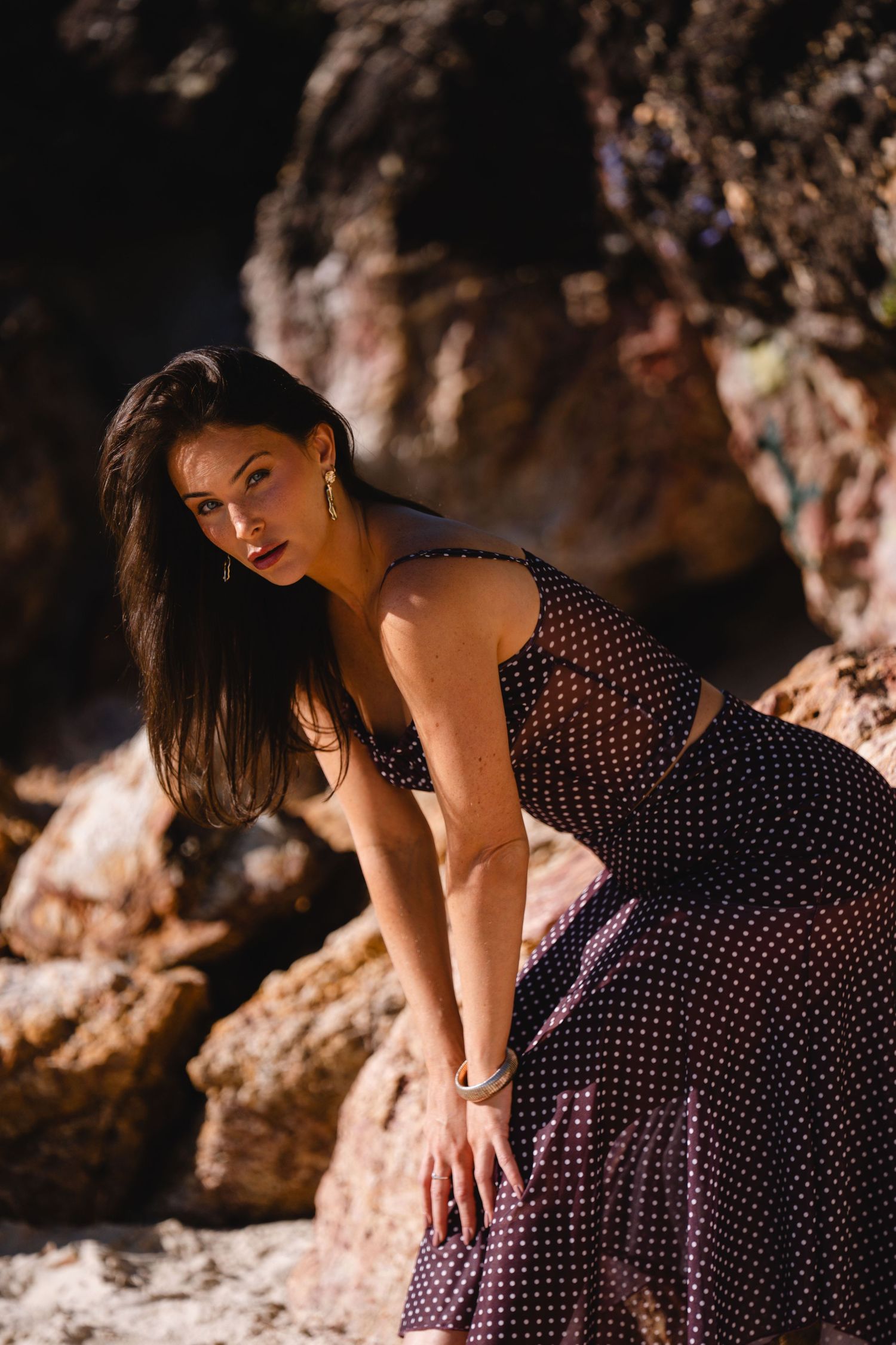 Artistic portrait in polka dot dress against dramatic cave lighting.