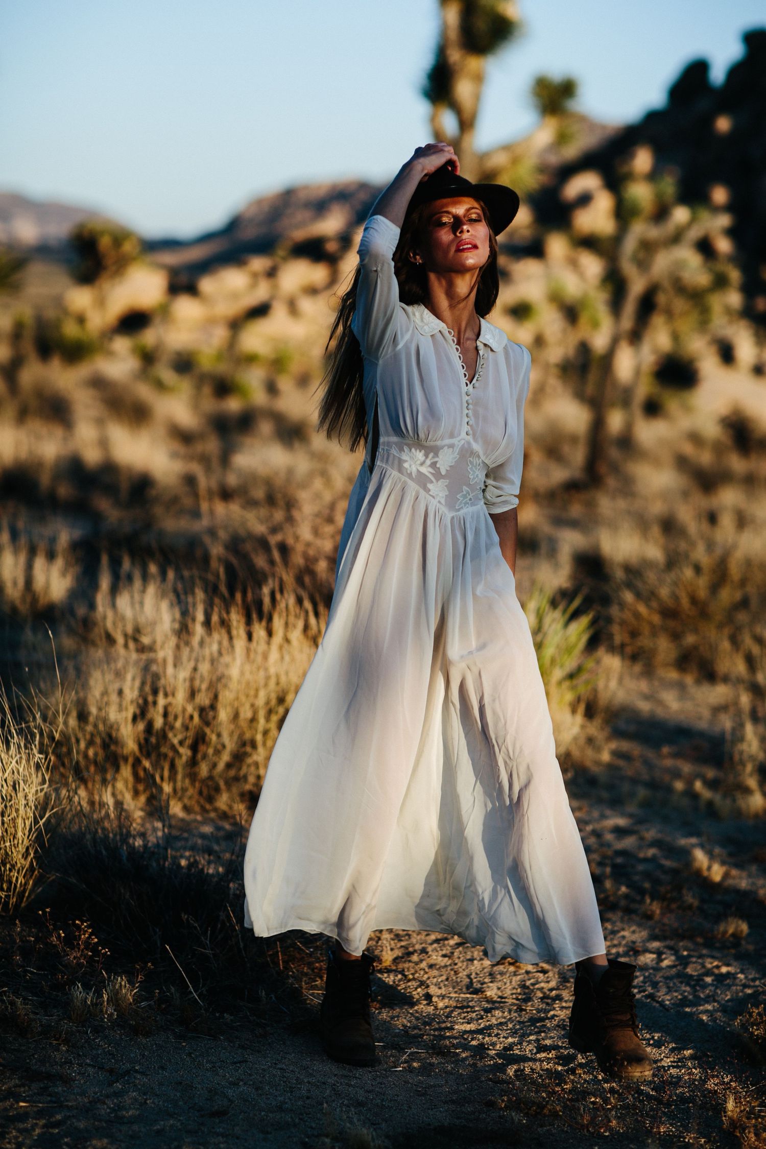 A white flowy dress moves gracefully in the desert landscape during golden hour with Joshua trees in the background.