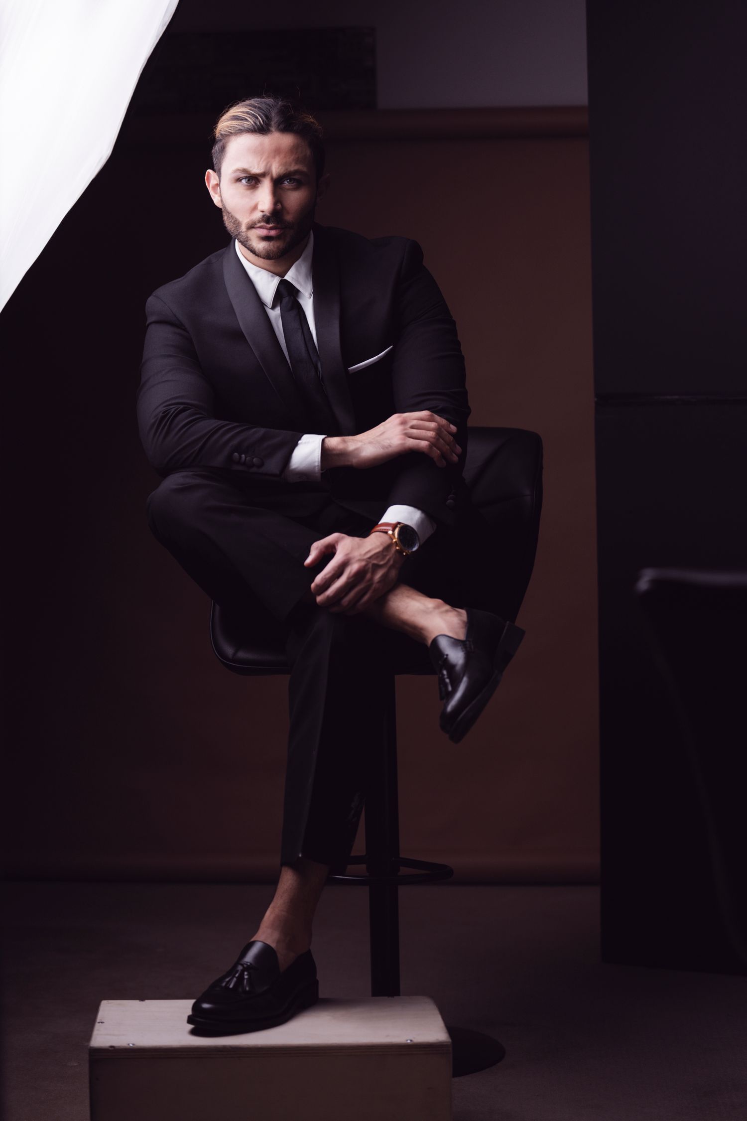 Dramatic studio portraits in black suit with moody lighting.