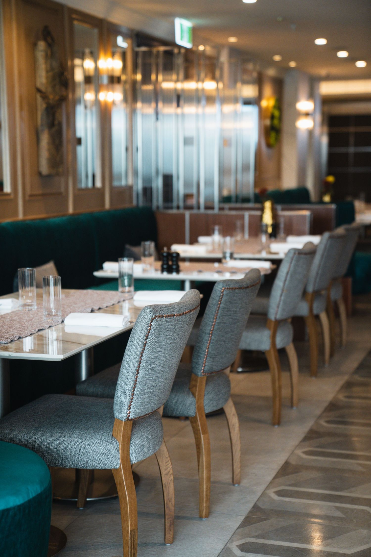 Modern restaurant interior with plush gray chairs and teal banquettes along marble tables in an elegant dining space.