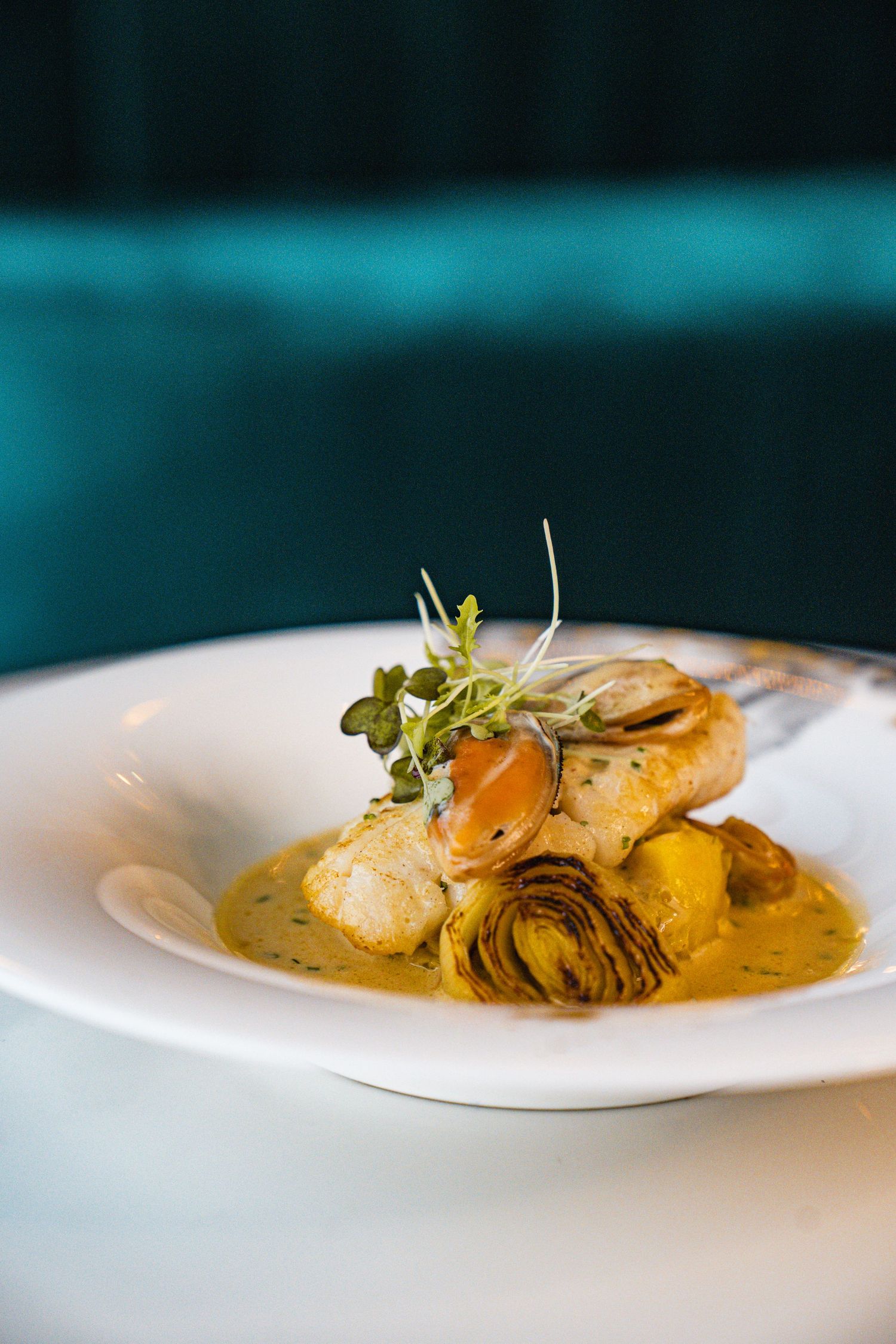 A series of plated dishes with artfully presented seafood in creamy sauce garnished with microgreens on white plates.