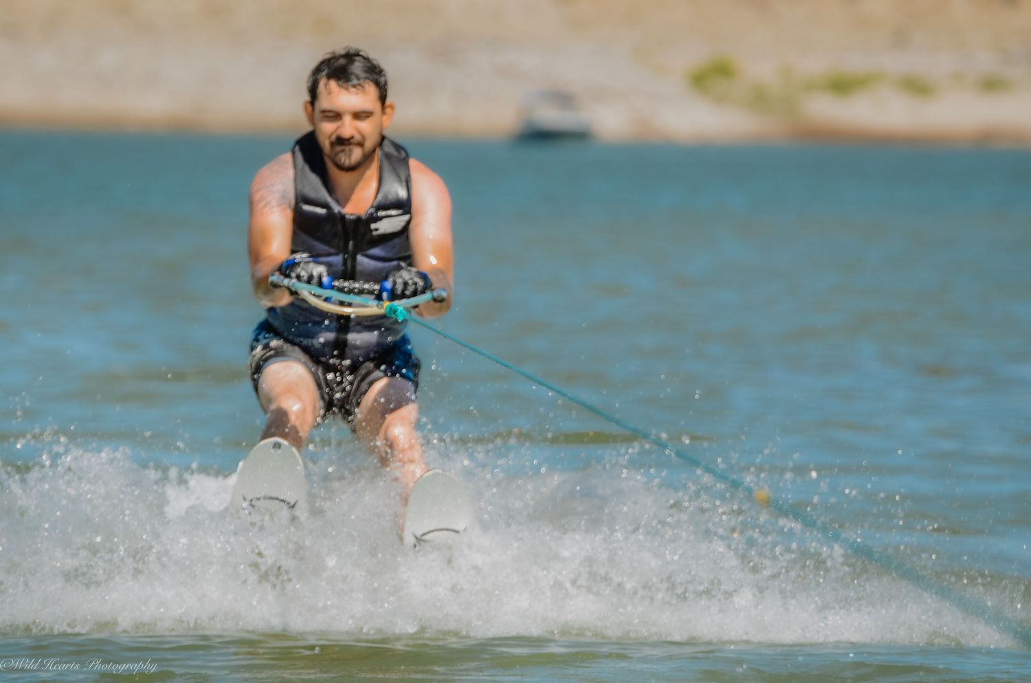 Action photograph of a man waterskiing across a lake, creating a splash while holding a tow rope during an outdoor water sports session.