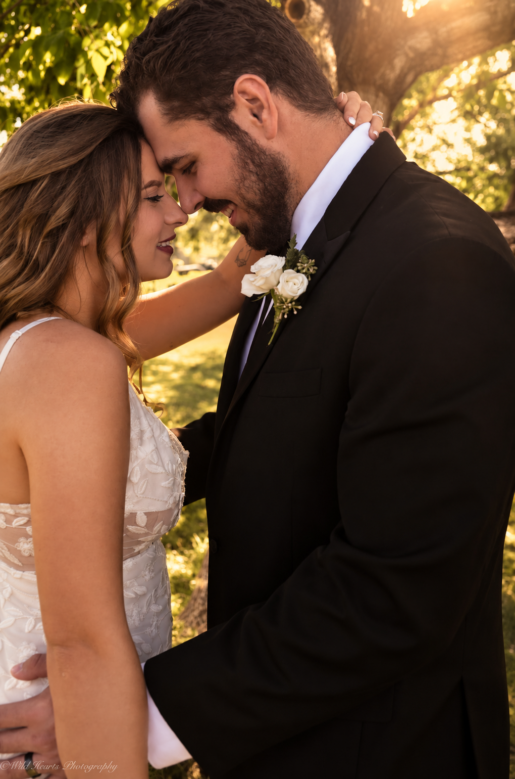 Romantic outdoor wedding portrait of a bride and groom touching foreheads beneath golden autumn trees during their wedding day.