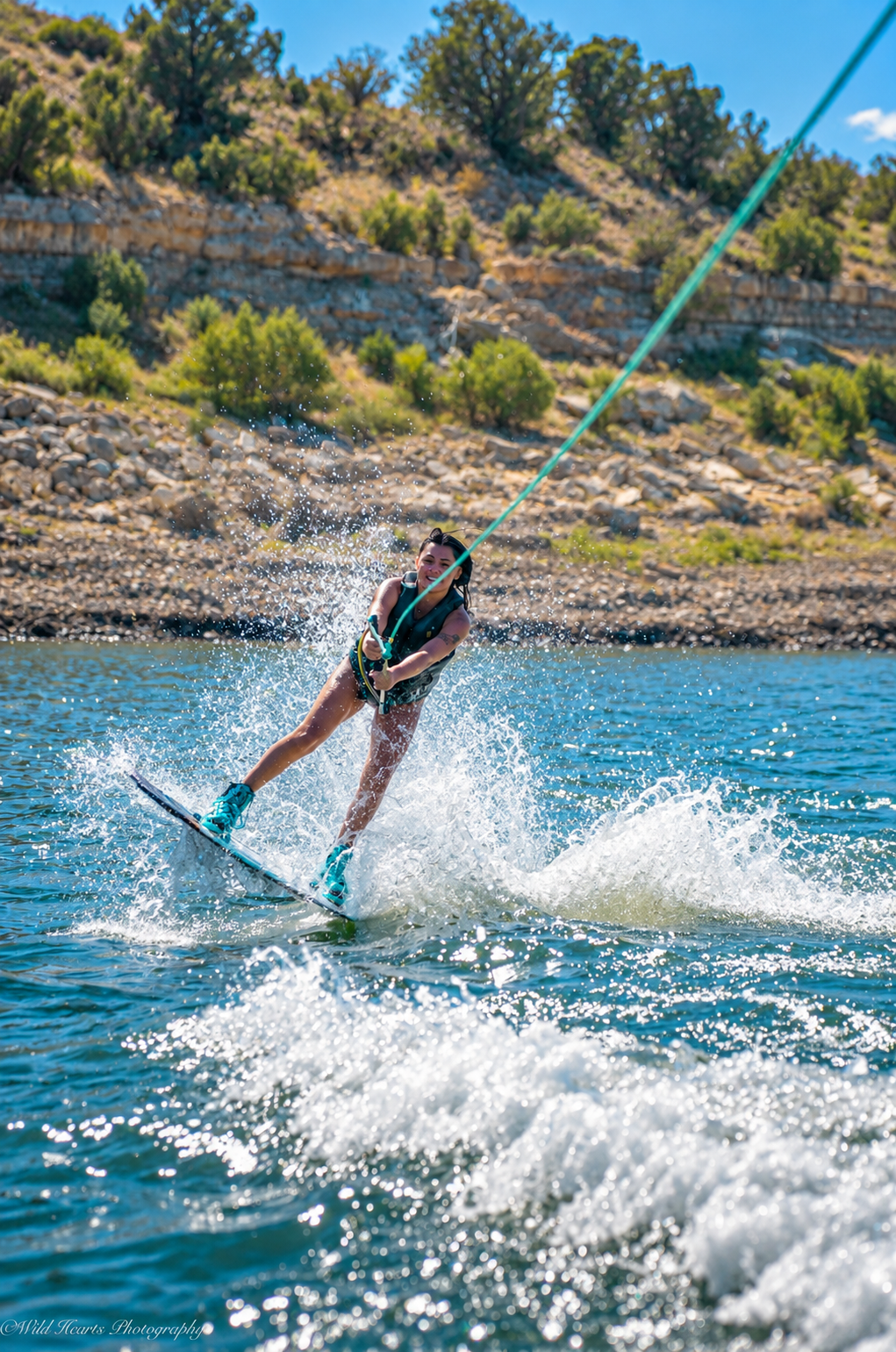 Outdoor action photograph of a woman waterskiing across a lake, leaning back on a tow rope with water spraying behind her.