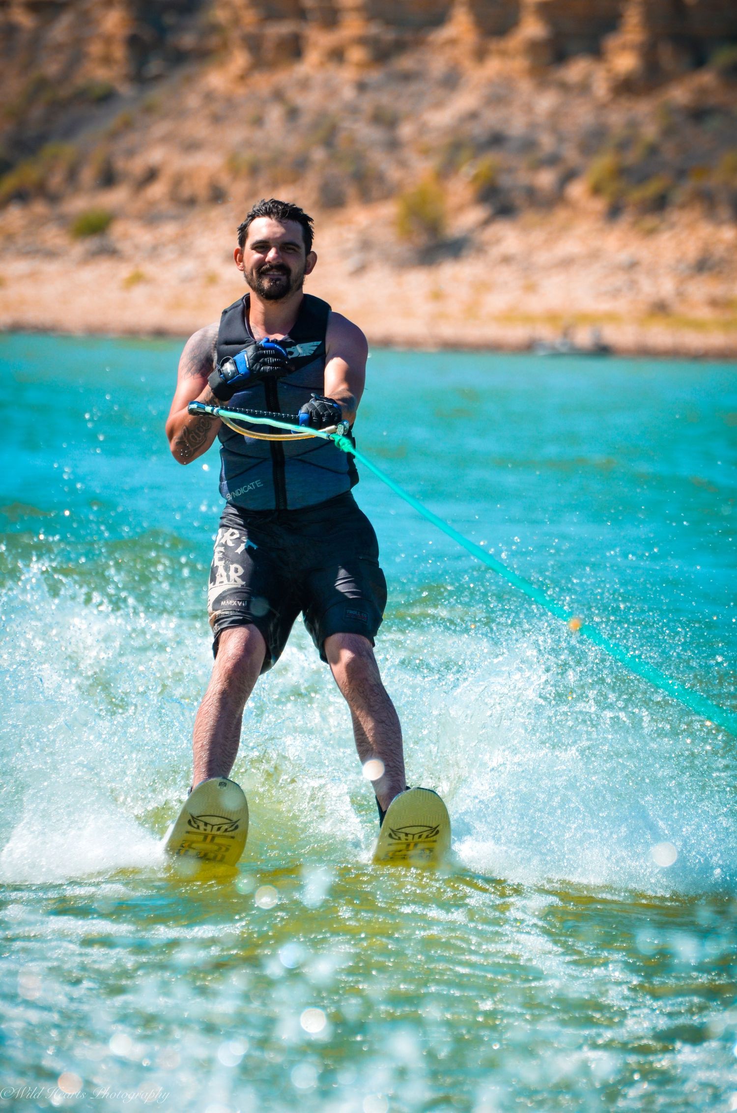 Action photograph of a man waterskiing across bright turquoise lake water, holding a tow rope with splashing water around his skis.