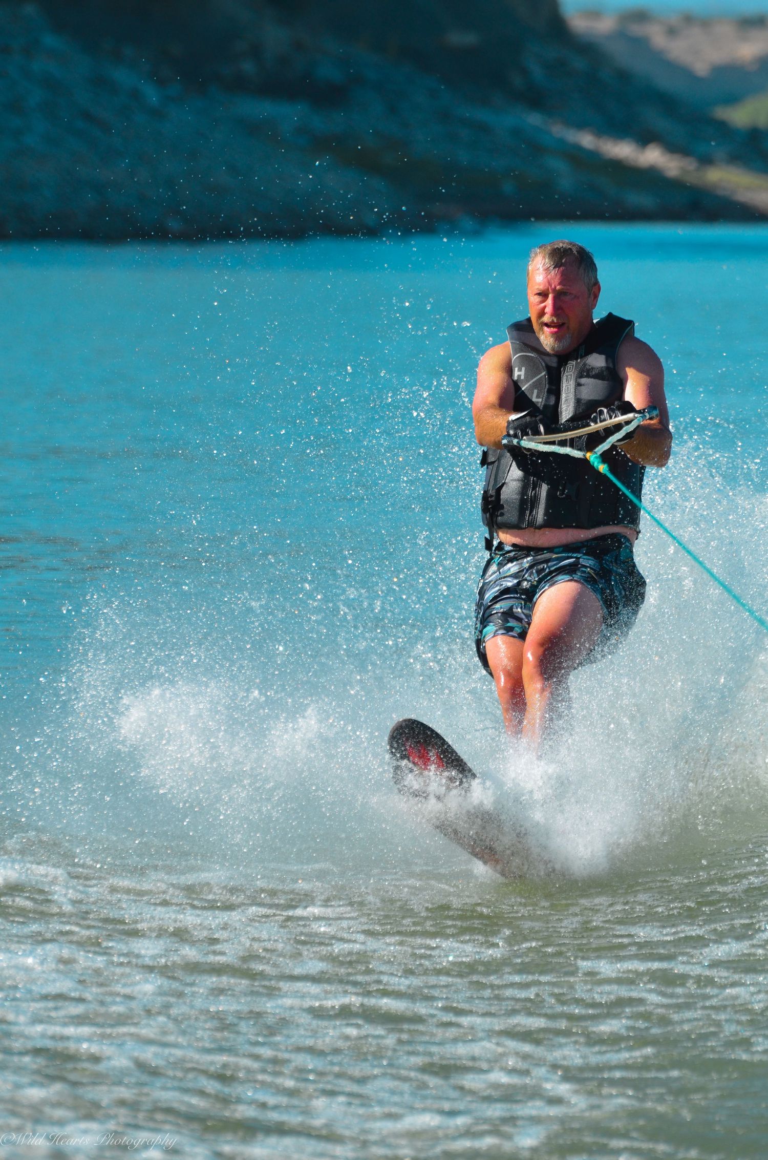 Watersports action portrait of a man skiing across a blue lake, creating a splash while holding a tow rope.