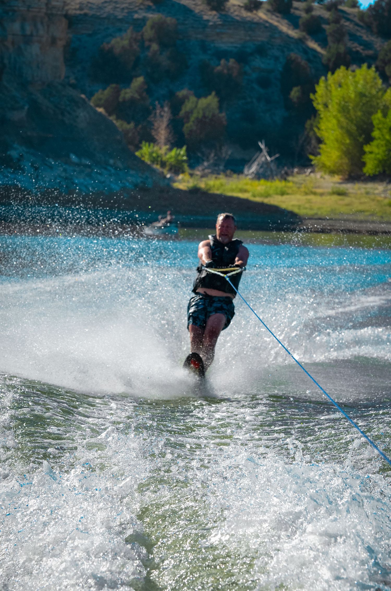 Action photograph of a waterskier gliding across a Colorado lake, creating a trail of spray with forested hills in the background.