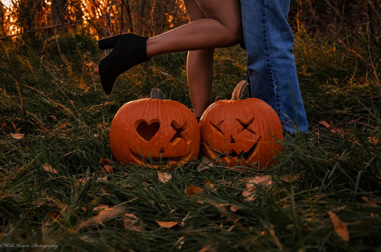 Dark romantic Halloween couples portrait featuring two people wearing carved pumpkin heads in a moody autumn forest.