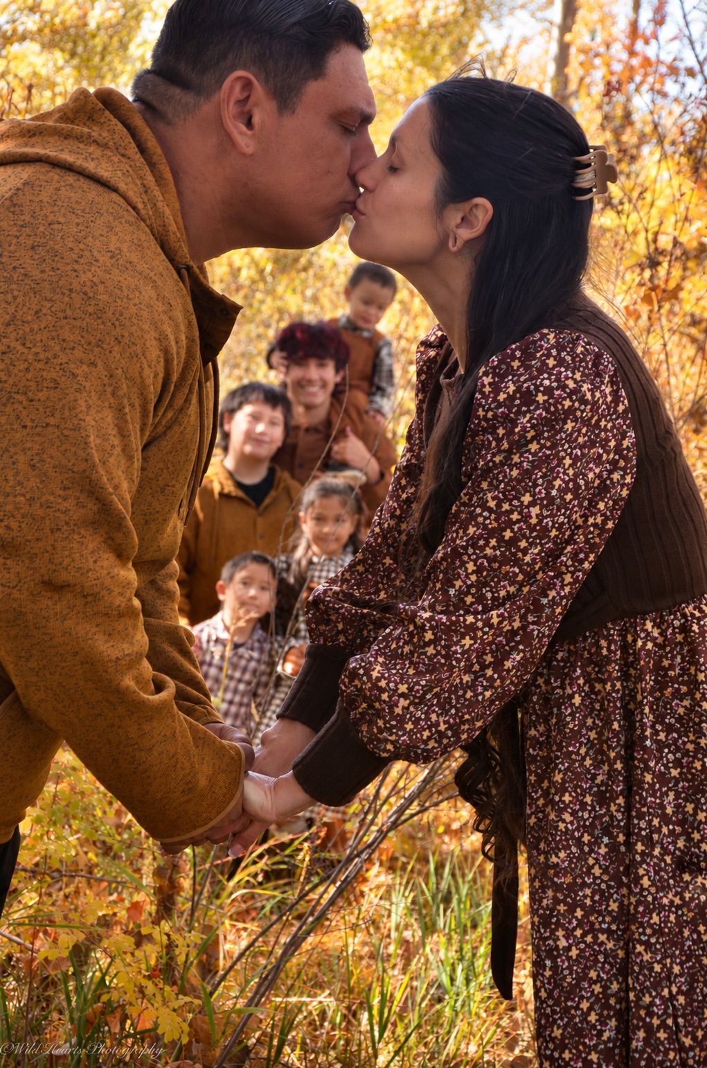Warm autumn family portrait of a couple holding their young child close while standing among golden fall leaves.