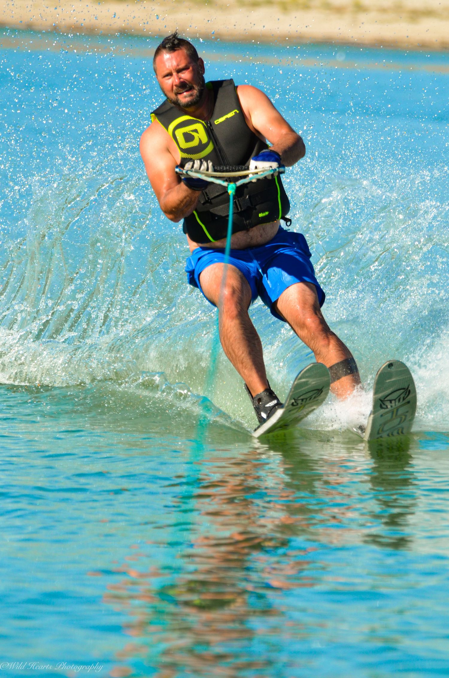 Waterskier balancing on the water while holding a tow rope, with bright blue lake water and splashing waves surrounding him.