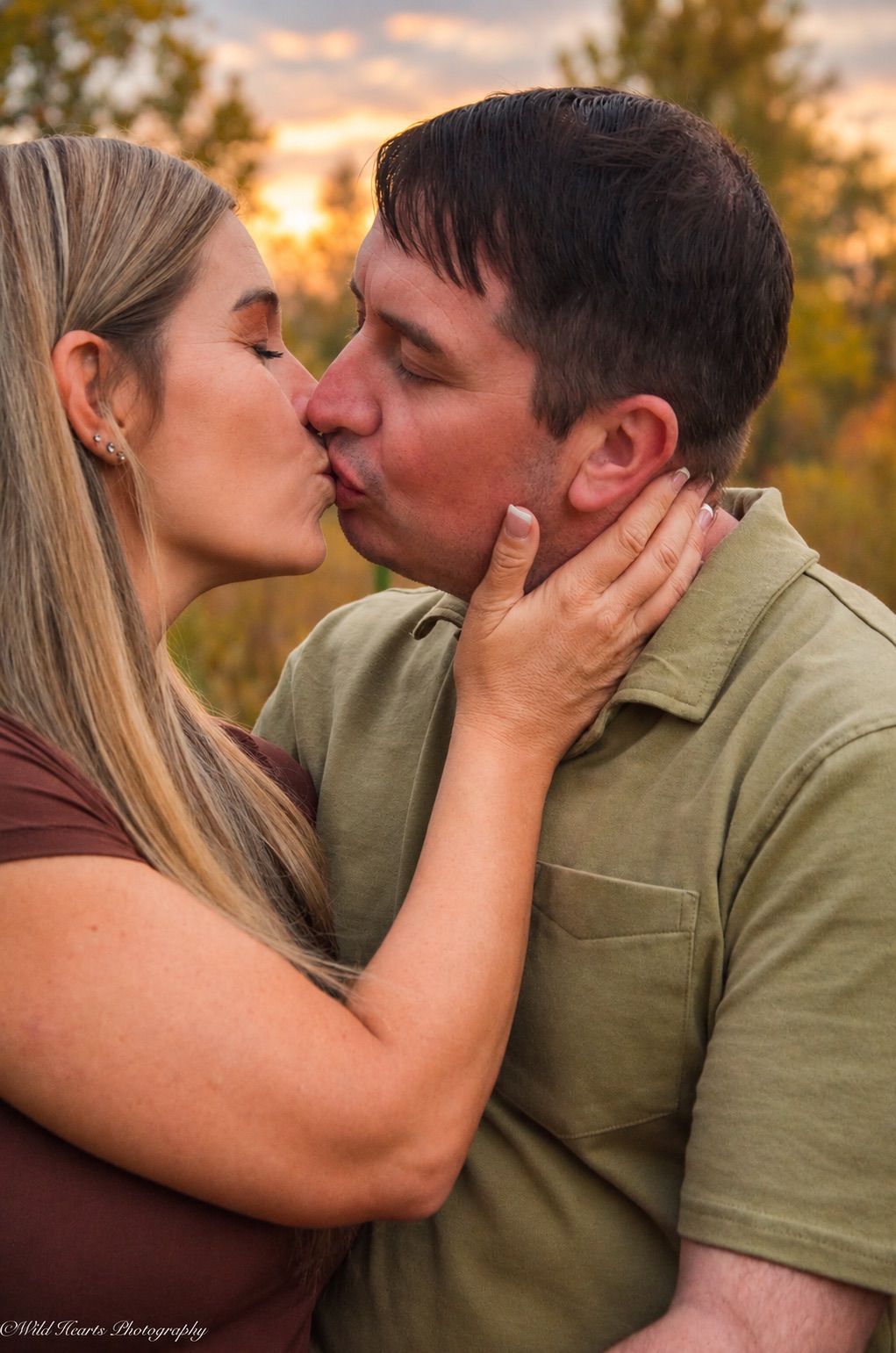 Romantic outdoor couples portrait of a man and woman sharing a kiss surrounded by warm autumn colors.