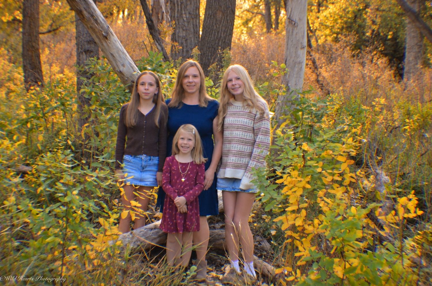 Outdoor family portrait of four standing together among golden autumn trees and colorful fall foliage in Colorado.