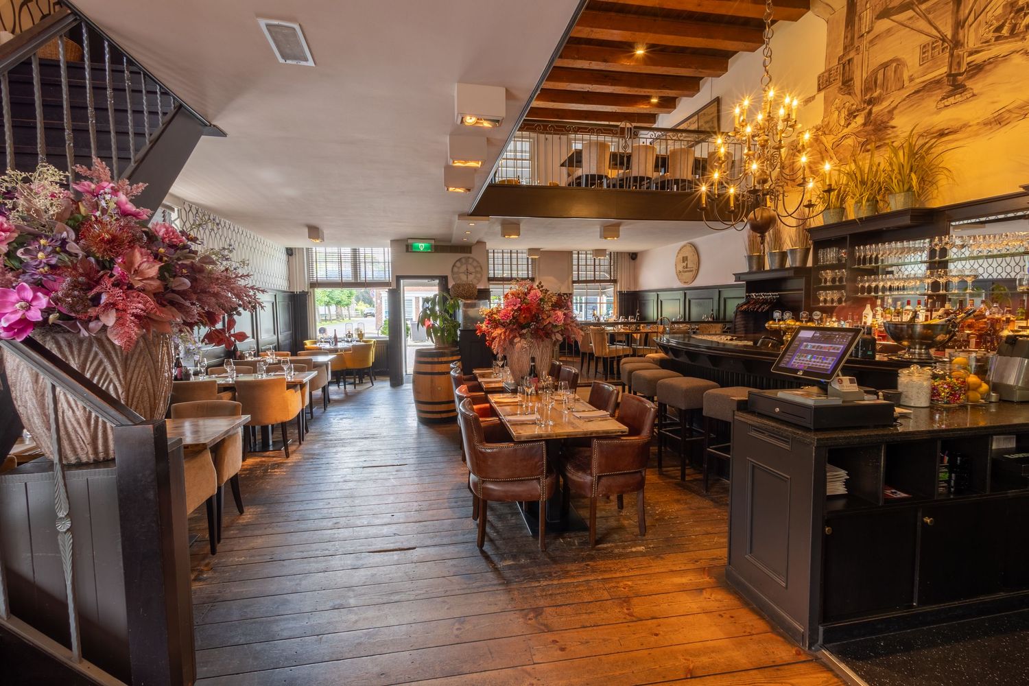 Upscale restaurant interior with warm wooden floors, elegant dining tables, and vibrant floral arrangements under ambient lighting.