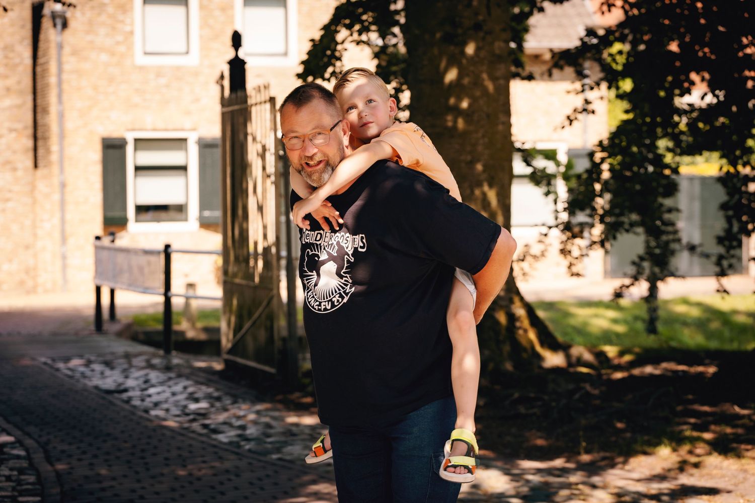 Two people share a sweet piggyback moment outdoors in warm sunset lighting on a cobblestone path.