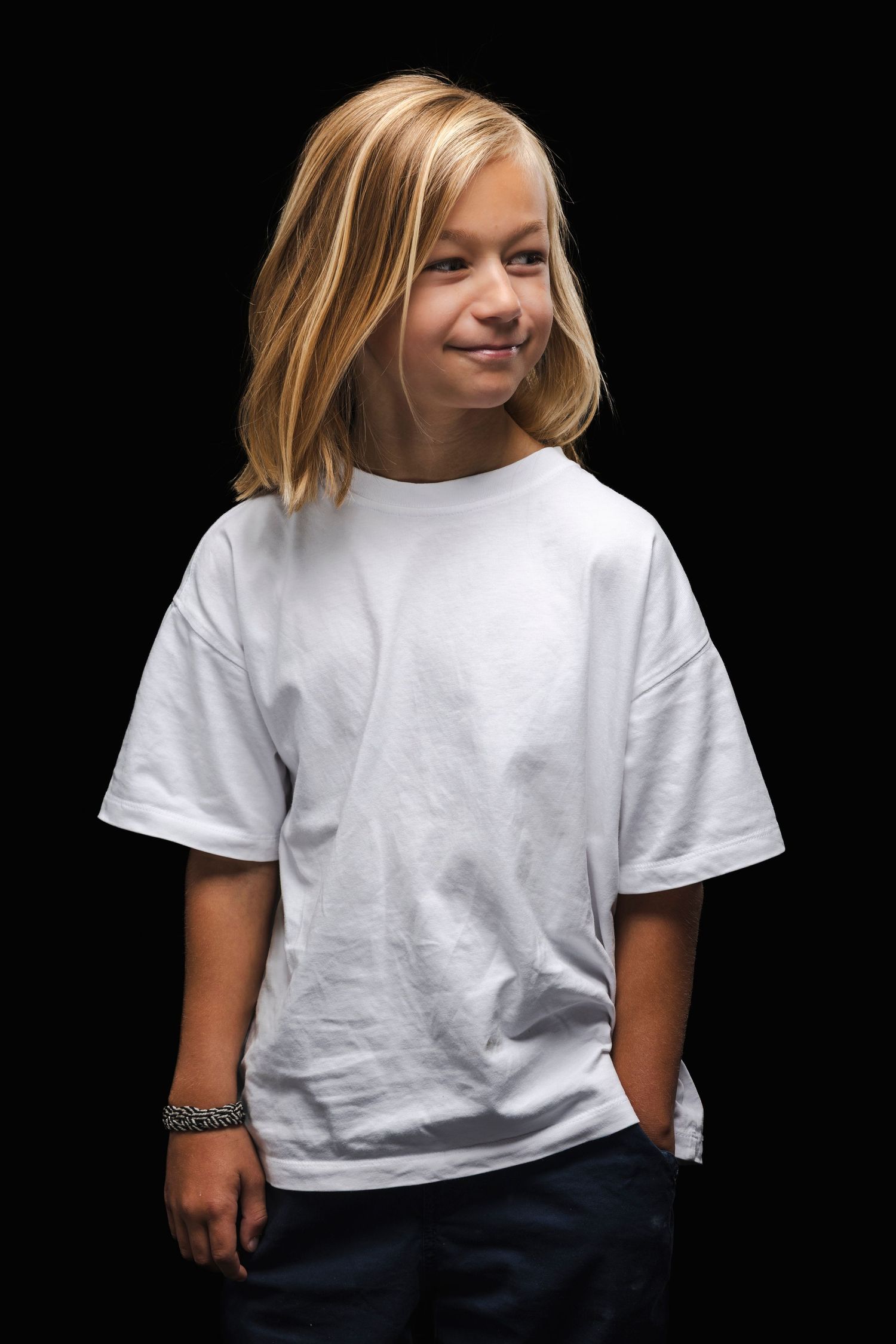 Young child wearing a casual white t-shirt and jeans smiles while posing against a black background.