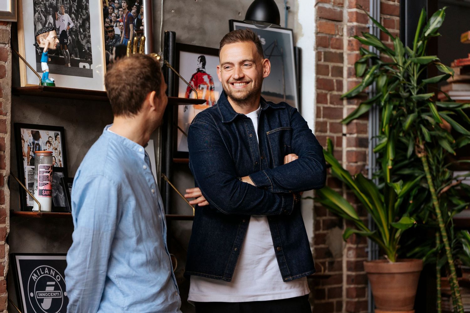 A group of people gathered informally near a brick wall with plants, having casual conversation.