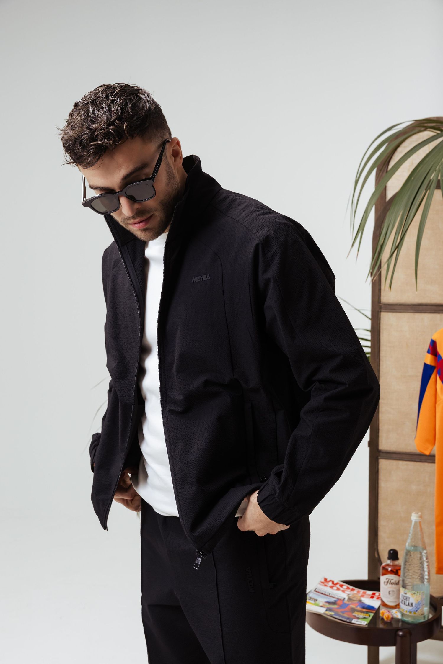 A person wearing a black jacket poses against a white background with orange accents visible in multiple angles.