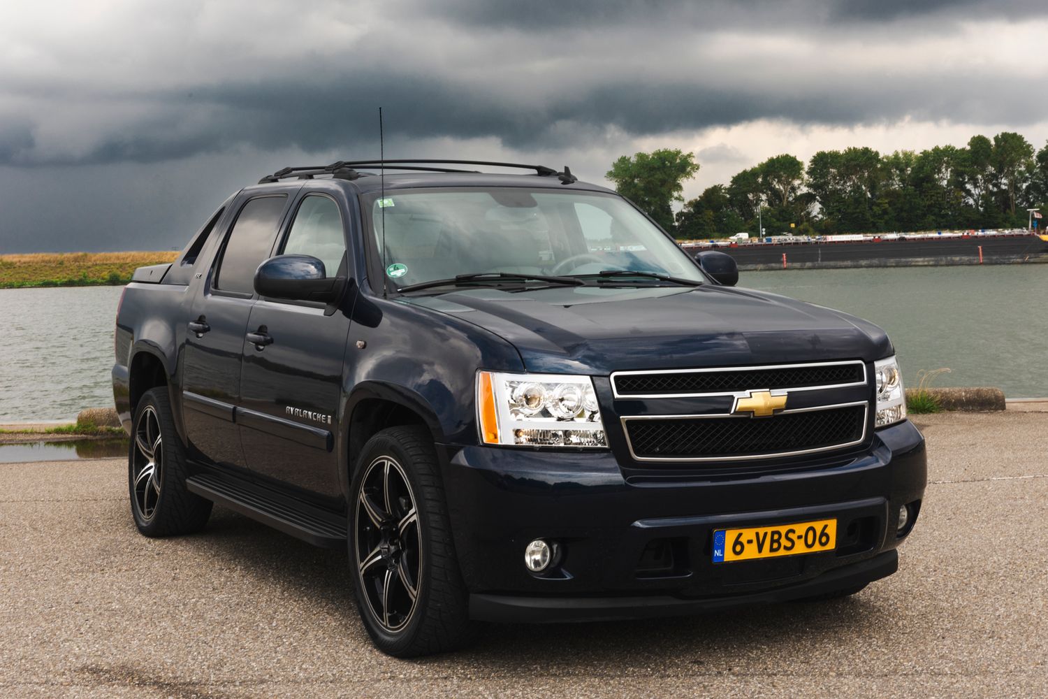 Several black Chevrolet Tahoe and Suburban SUVs in different poses on a road with dramatic cloudy skies.