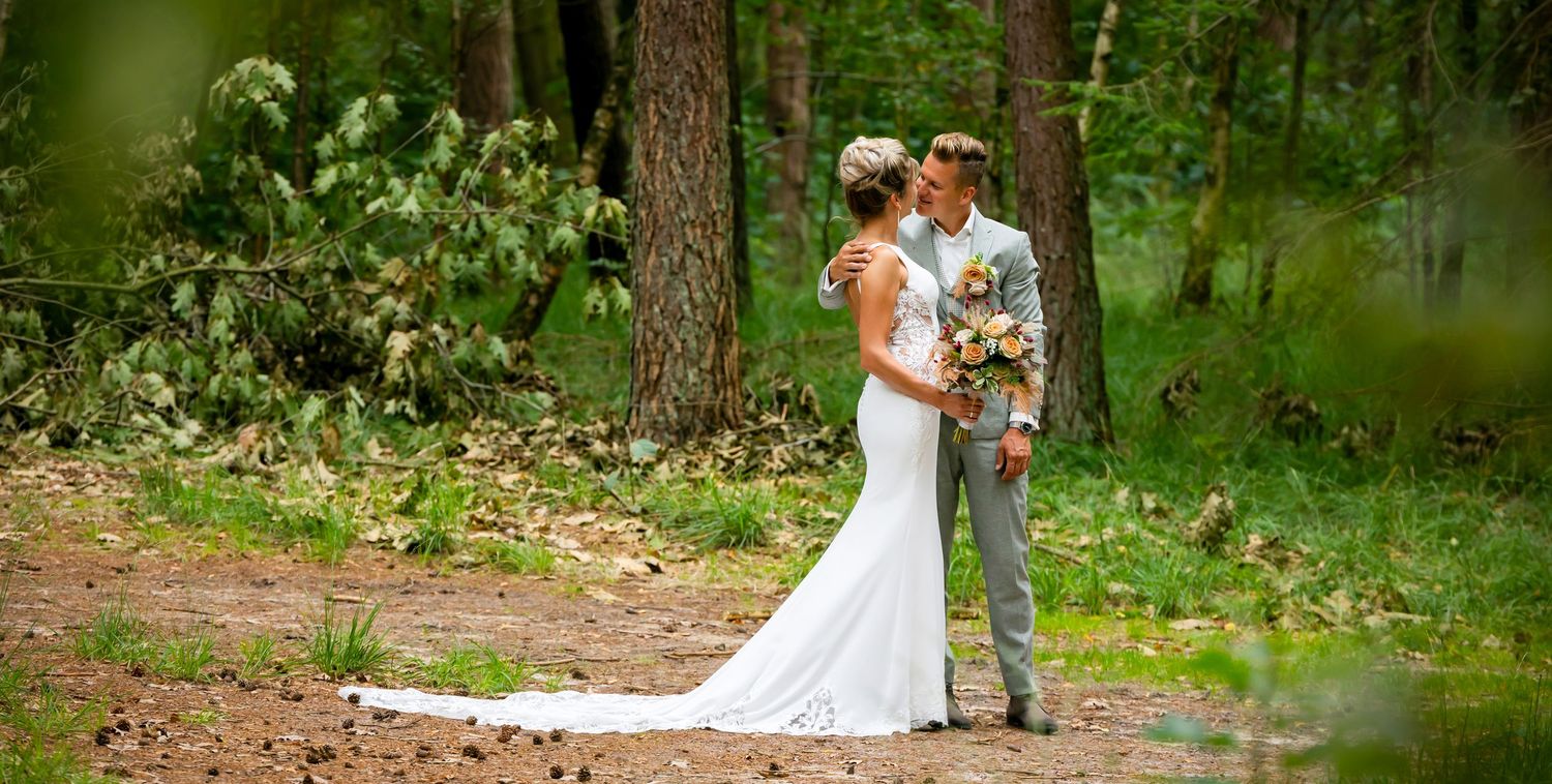 A couple in wedding attire shares a tender moment among trees in a lush forest setting.