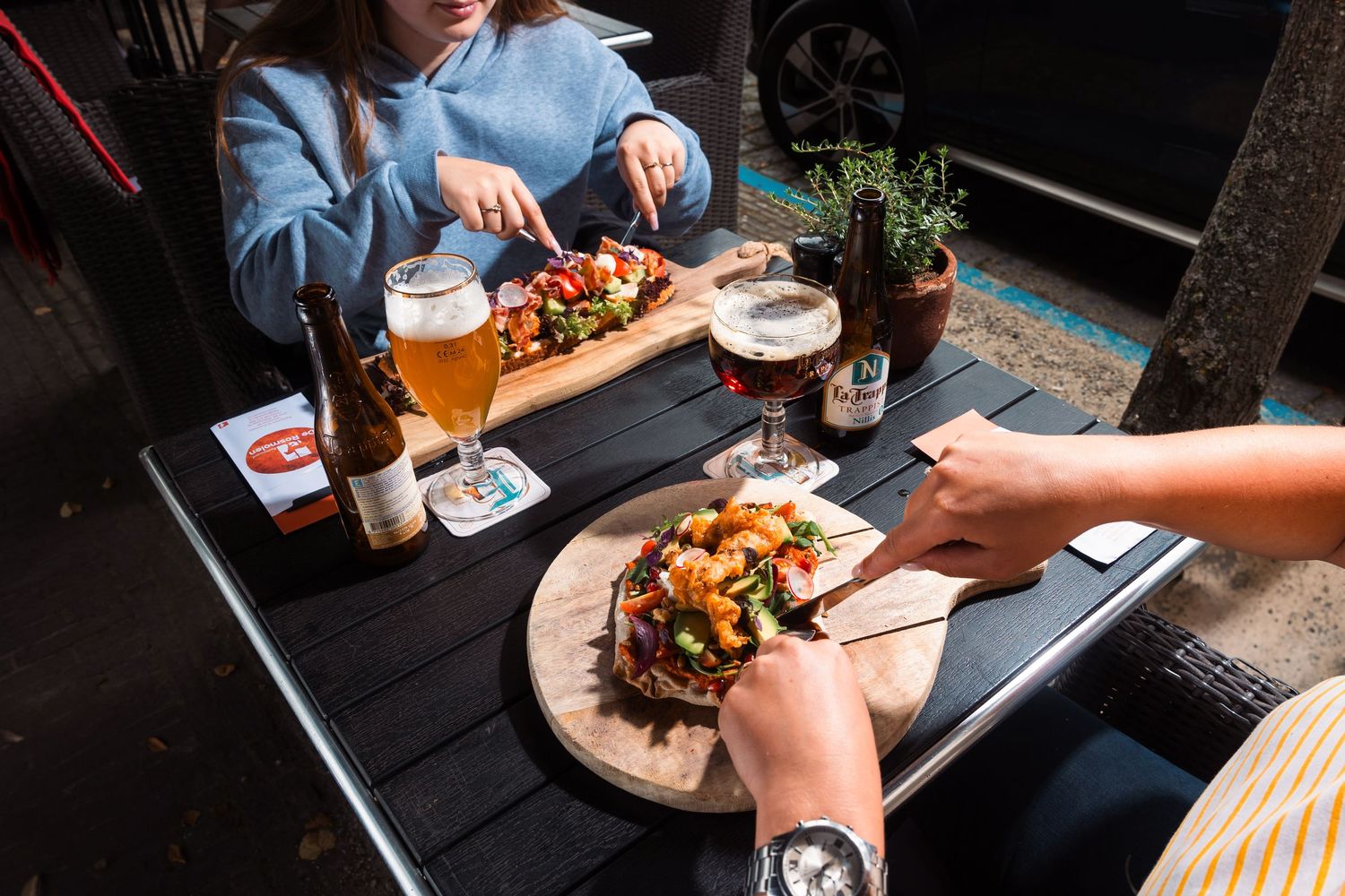 People enjoying craft beers and shared plates of food at a casual restaurant table with wooden serving boards.