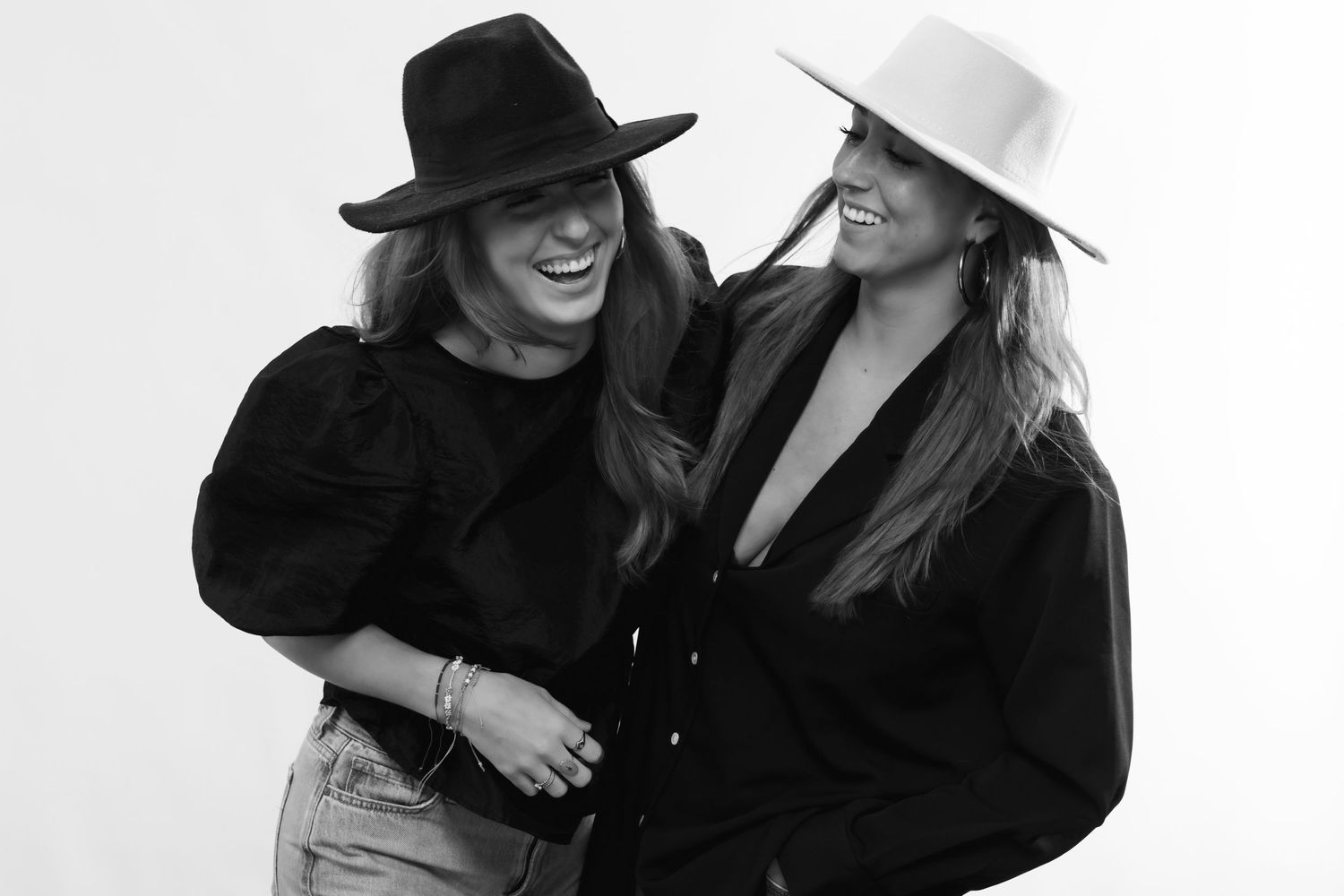 Two people in contrasting black and white hats share a candid laughing moment in a black and white photograph.