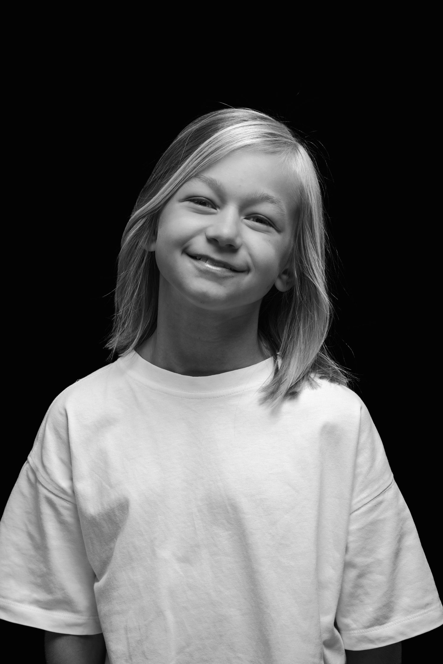Black and white portrait of a young person in a white t-shirt smiling warmly at the camera.