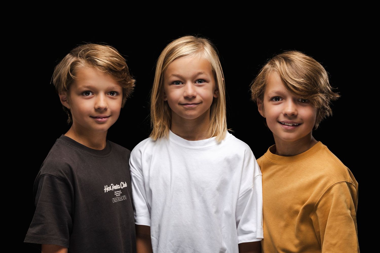 Three young children smiling and posing together in casual clothing.