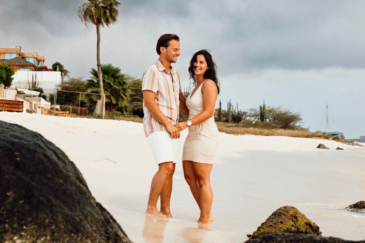 Romantic beach photoshoot with waves crashing against rocks in the background.