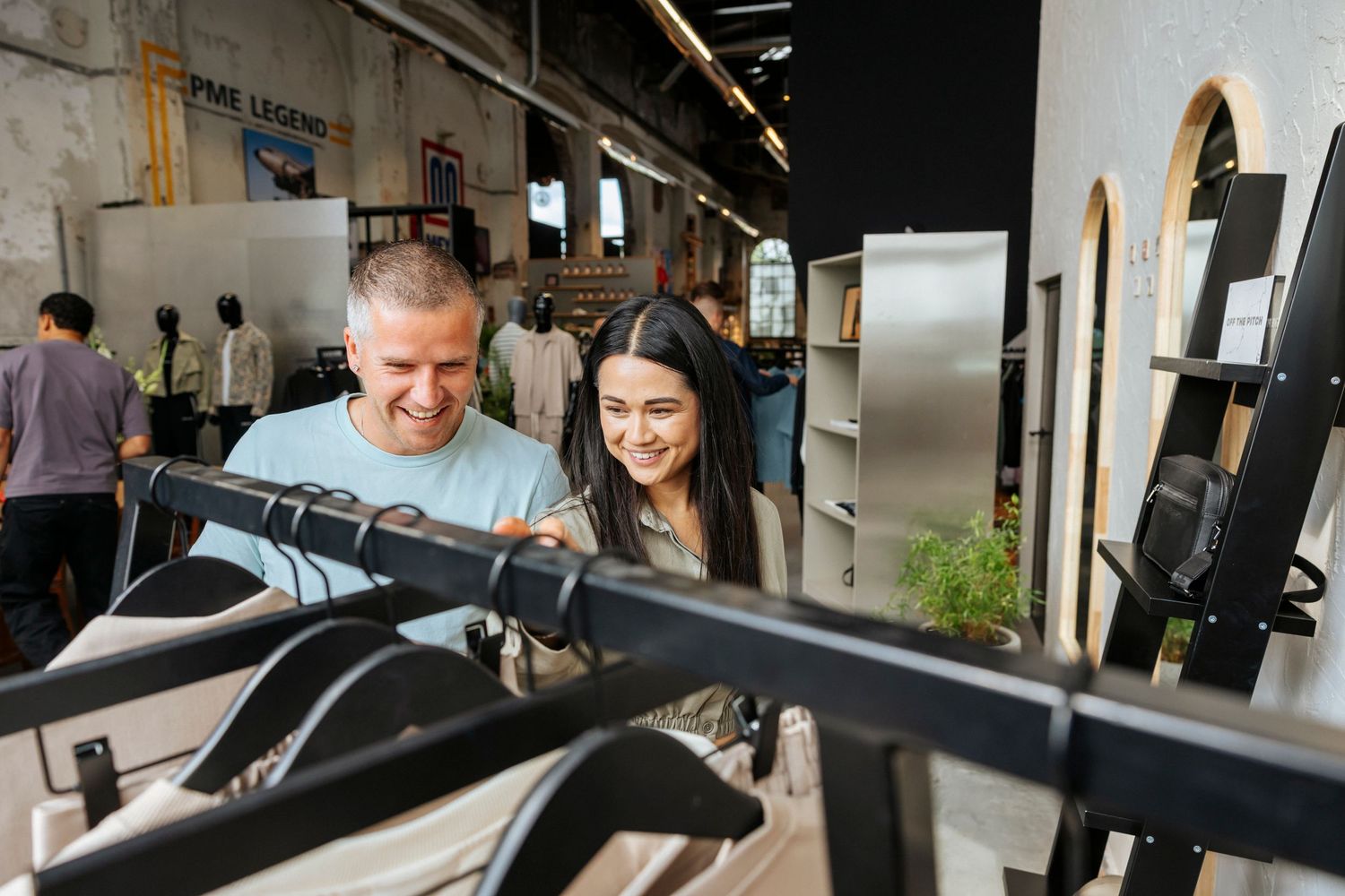 Two people exercise and work out together on machines in a modern gym facility with natural lighting.