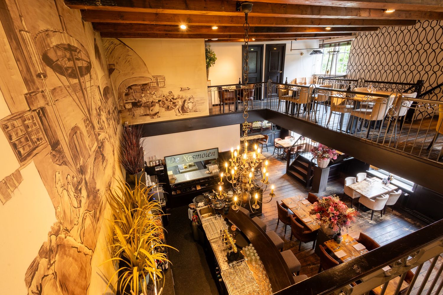 Modern restaurant interior with mural artwork, elevated dining area, and bar counter illuminated by warm lighting.