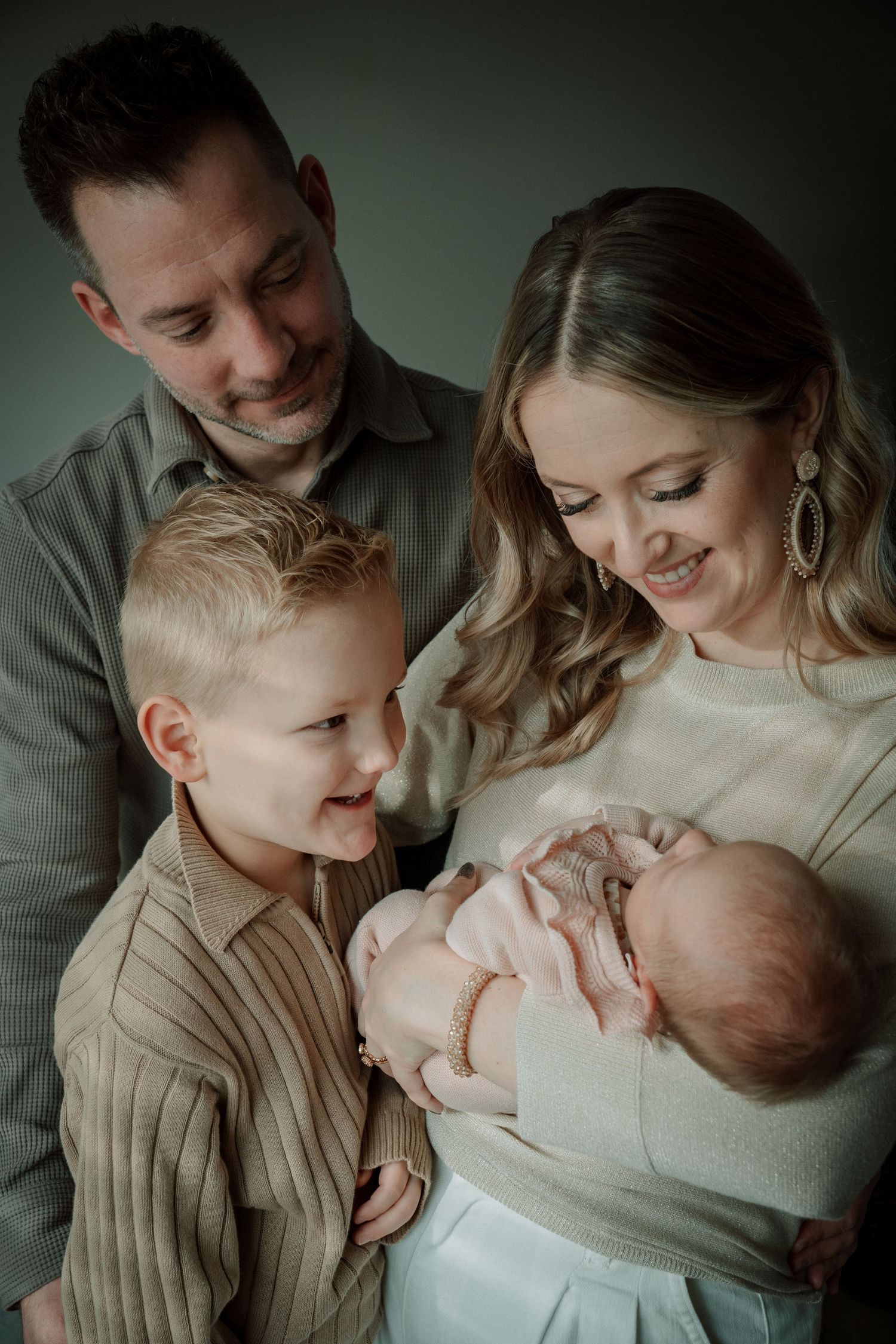 A family shares an intimate moment together as they gather around their newborn baby in a moody studio portrait.