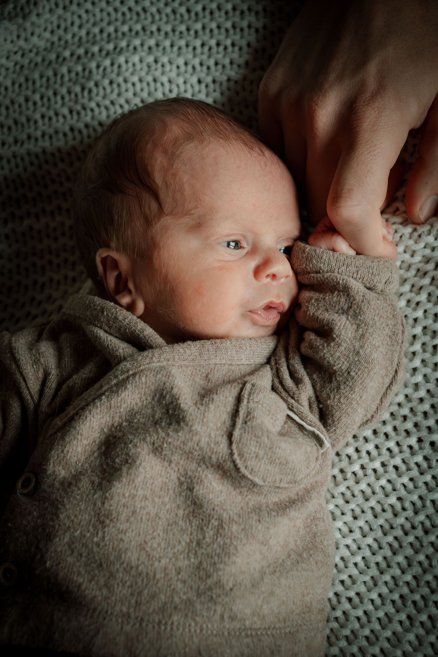 A sleeping newborn baby wrapped in a soft gray blanket rests peacefully on a knitted white blanket.