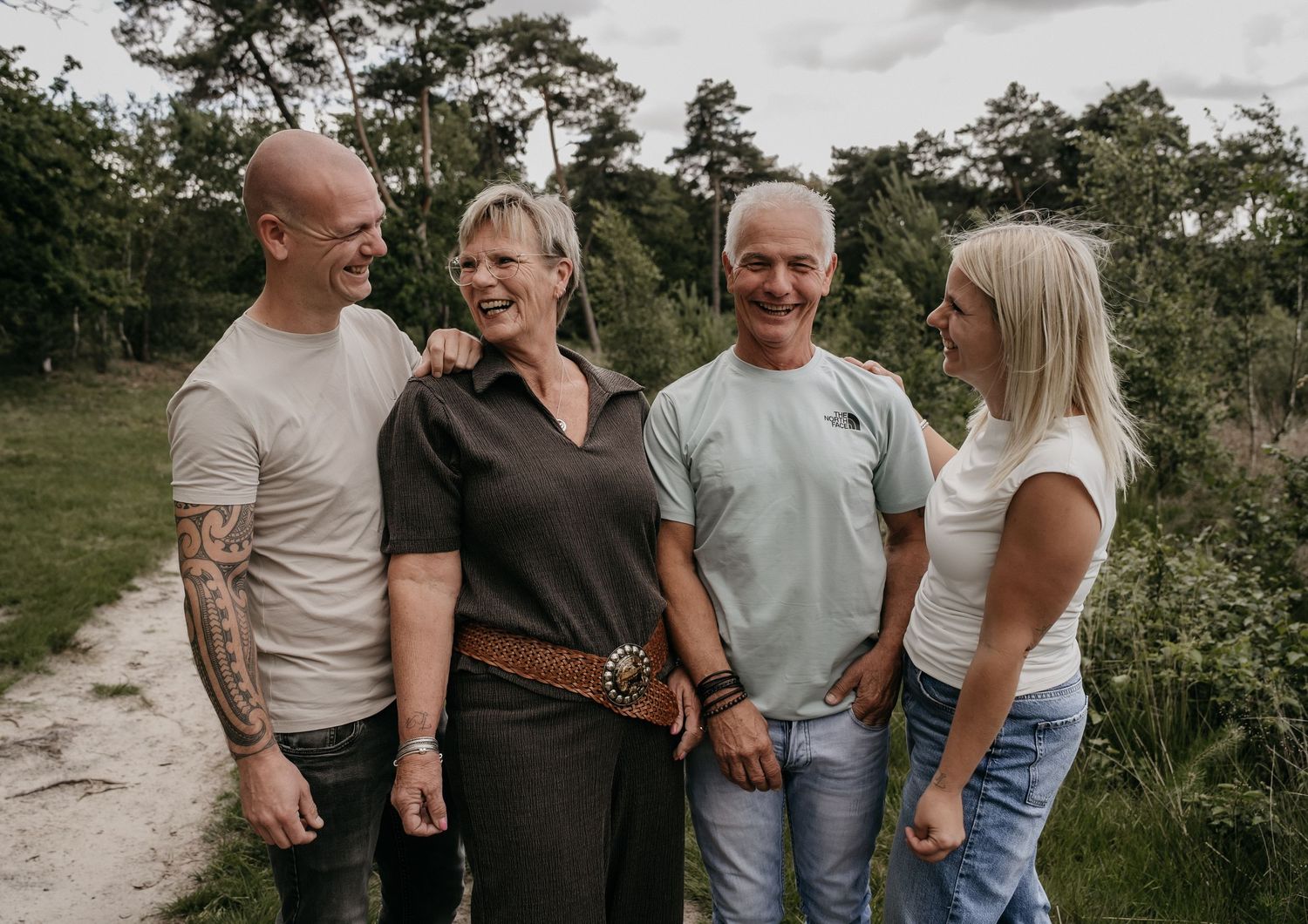 Four smiling adults posing together outdoors in a lush green nature setting on a sunny day.