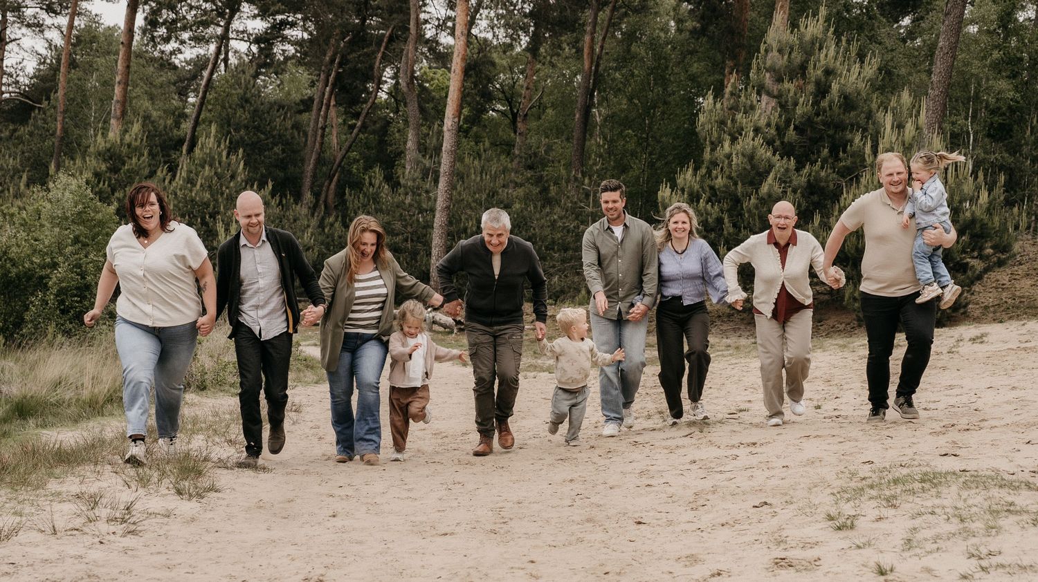 Large multigenerational family walking together on a sandy forest path, smiling and holding hands outdoors.