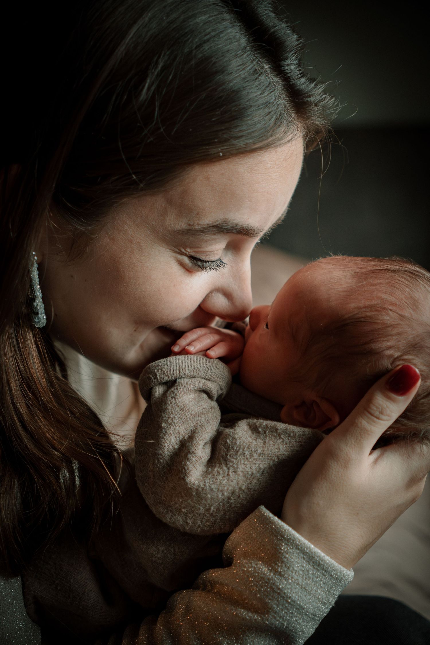 A tender moment captured in moody lighting as parent and baby share an intimate bonding moment with a teddy bear.