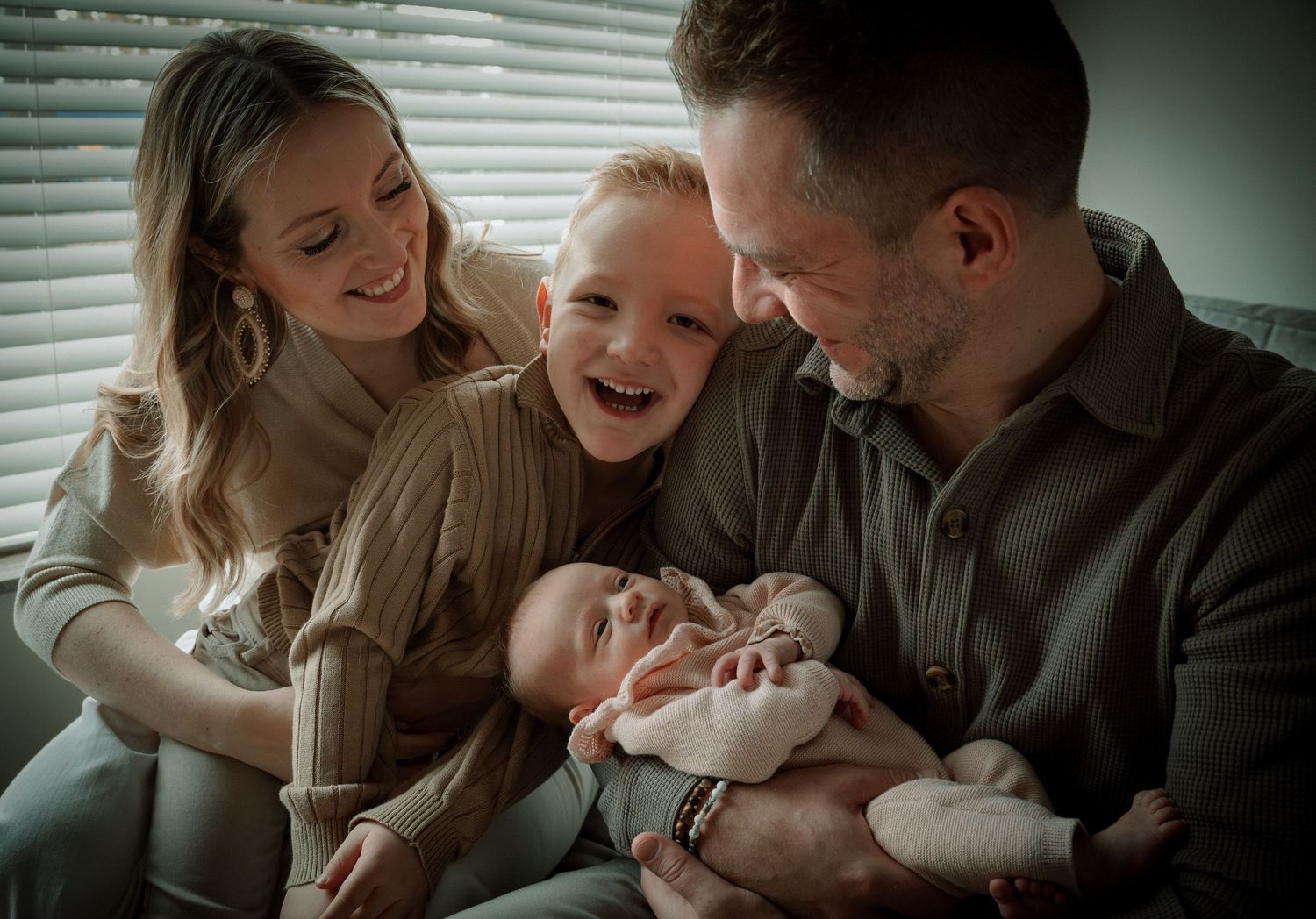 A family shares joyful moments together while relaxing on a couch in natural lighting.