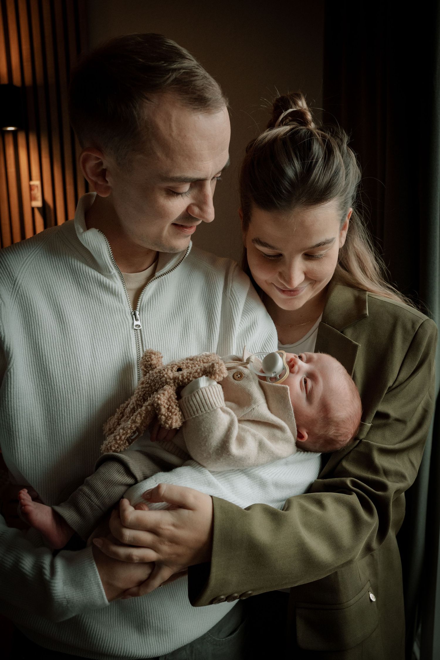 A couple in white and olive clothing share tender moments with their newborn baby in a series of intimate photos.