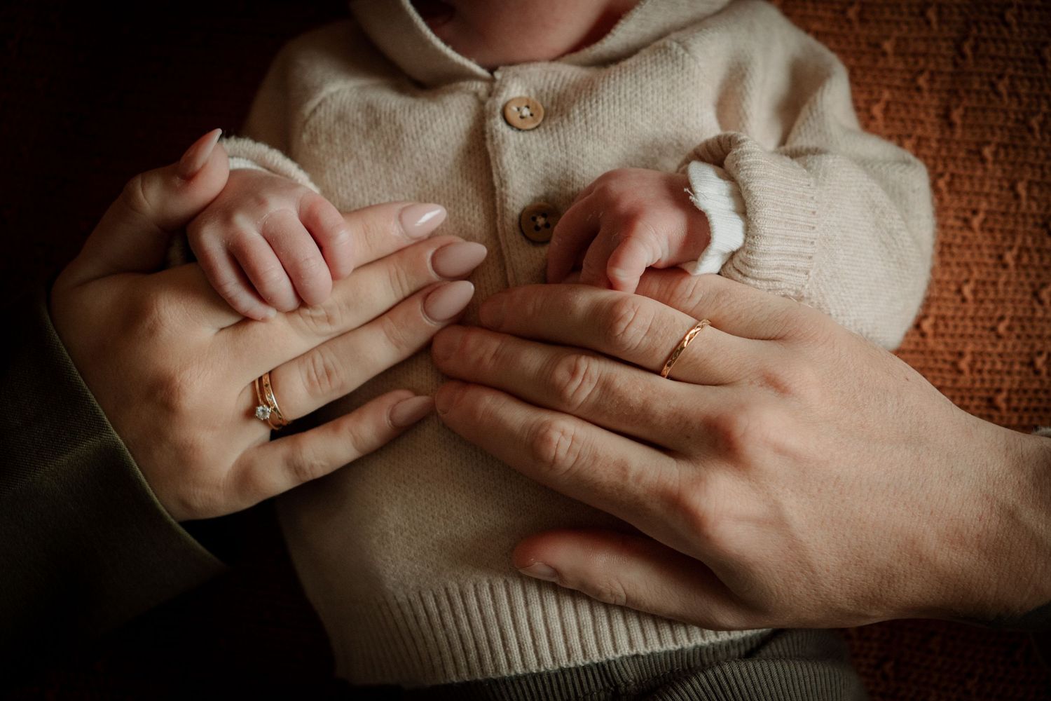 Hands crossed over heart wearing cream colored sweater against dark textured background.