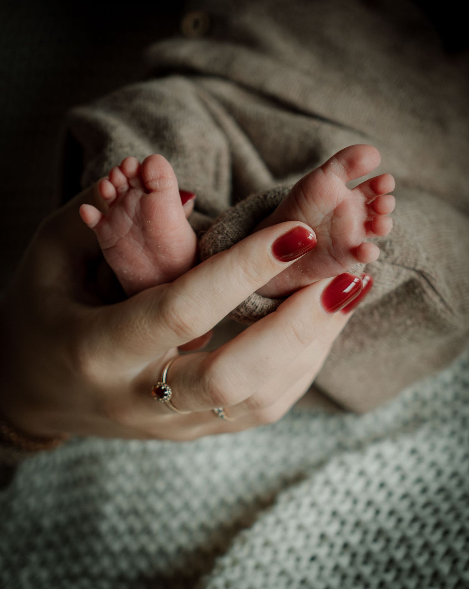 Close-up shot of tiny baby toes with red nail polish on a soft knitted blanket.
