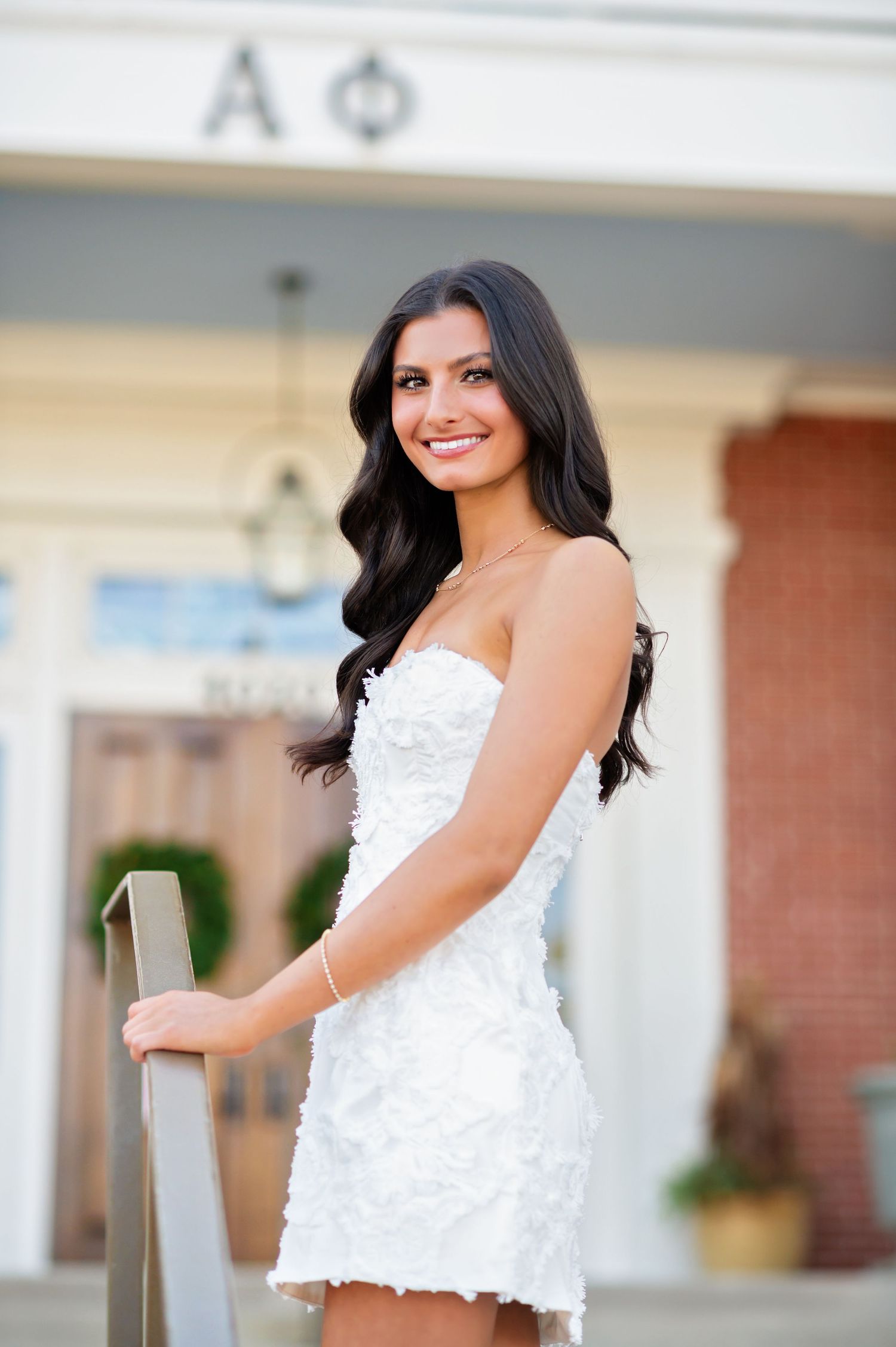 Young woman in white strapless dress smiling at Alpha Phi sorority house.