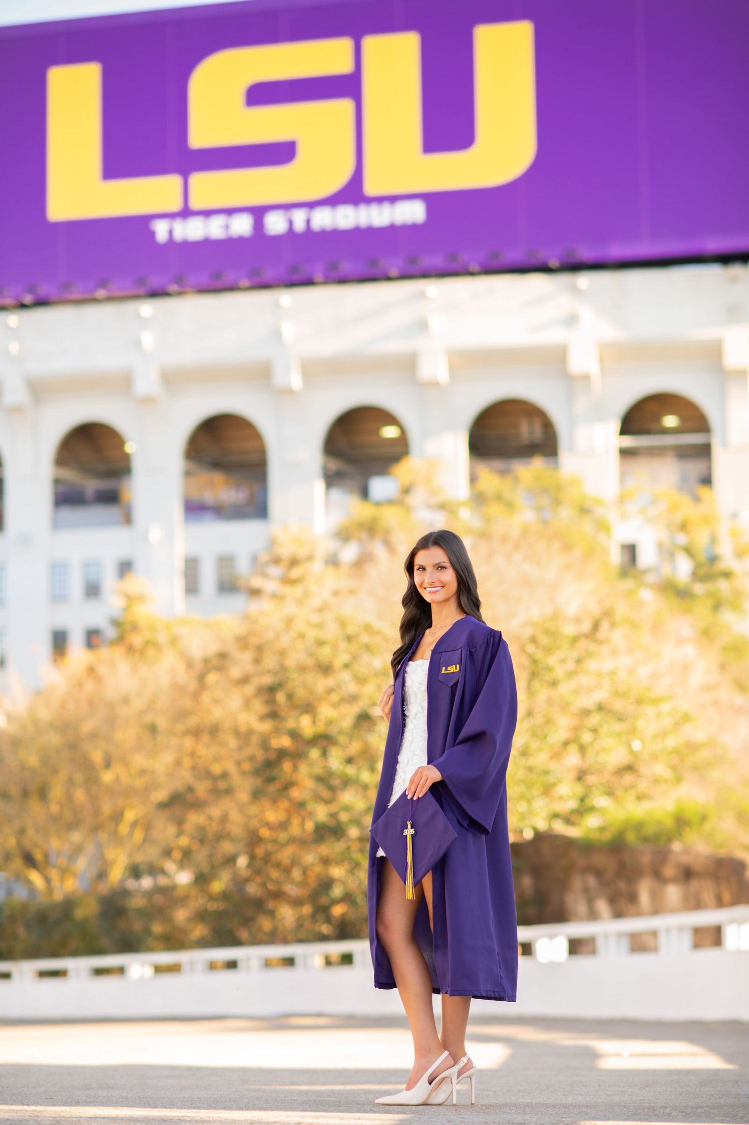 LSU graduate poses in purple cap and gown outside Tiger Stadium in Baton Rouge, Louisiana.