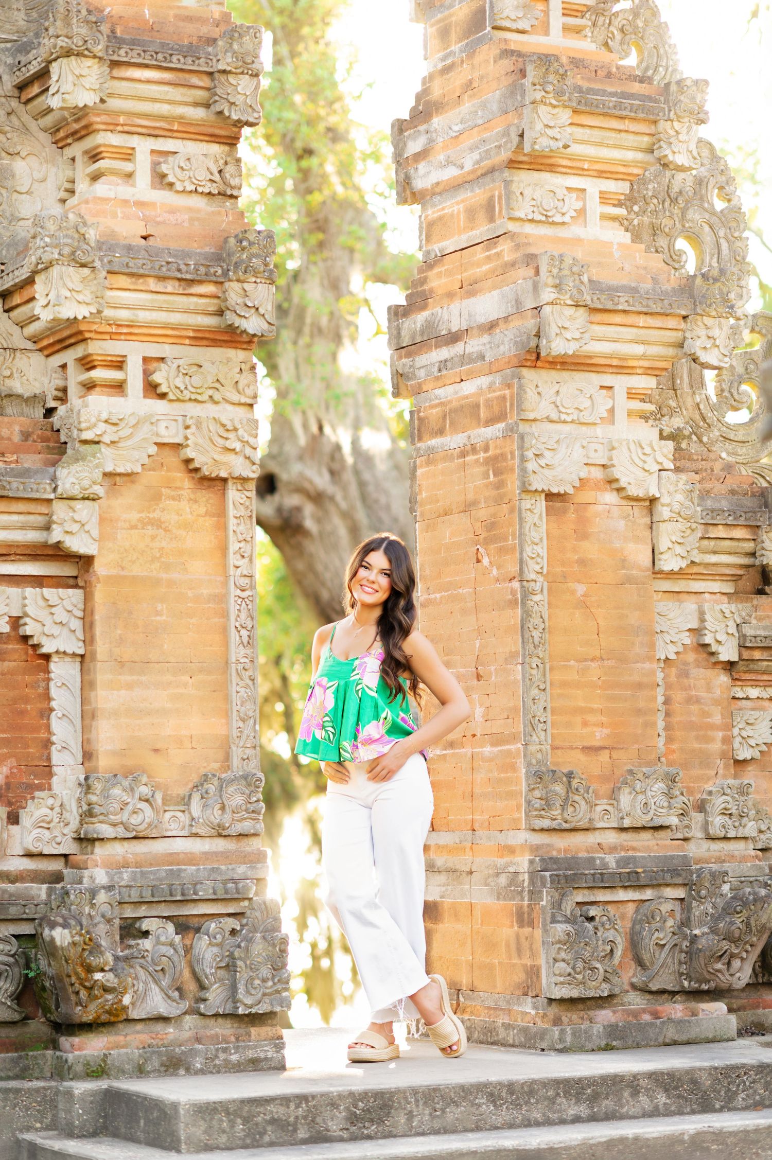 Woman in green top and white pants posing at ornate Balinese temple gate entrance.