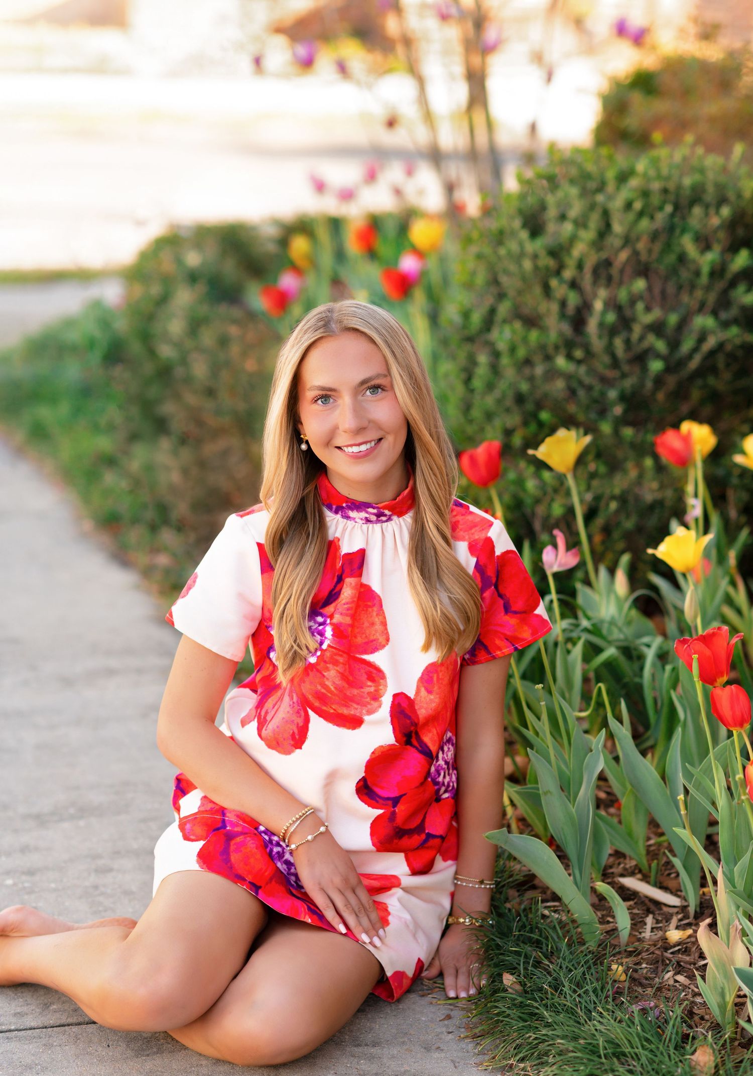 Young woman in floral dress sitting by colorful tulips in a garden path during golden hour.