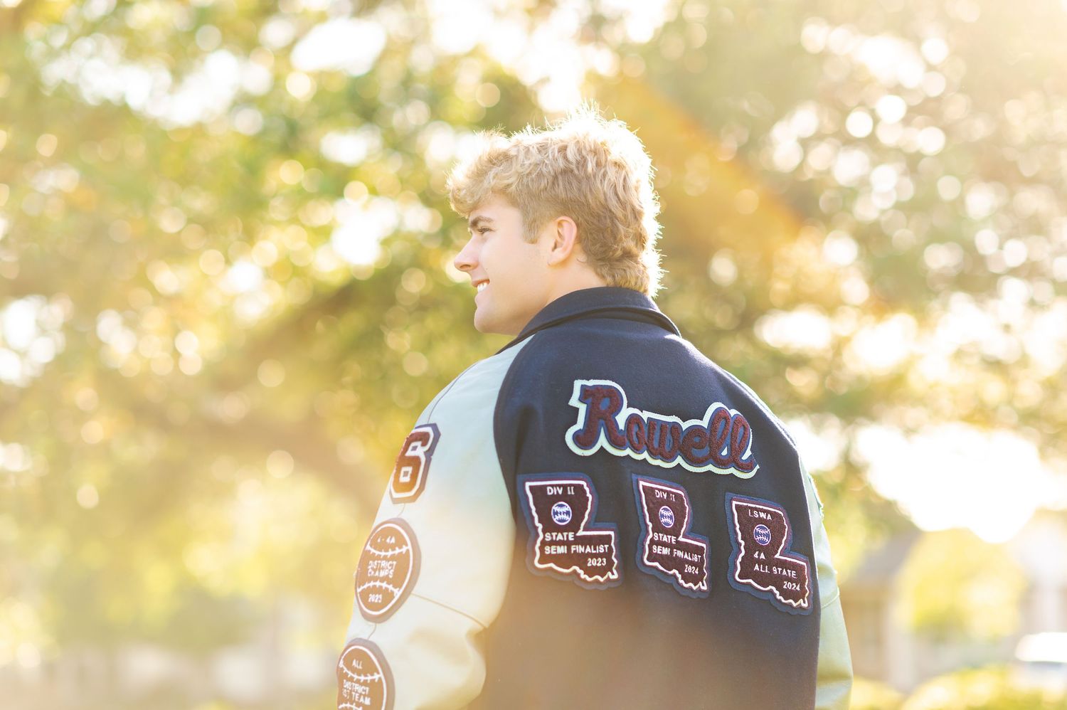 Blonde teen wearing a Rowell letterman jacket photographed from behind in golden autumn light.