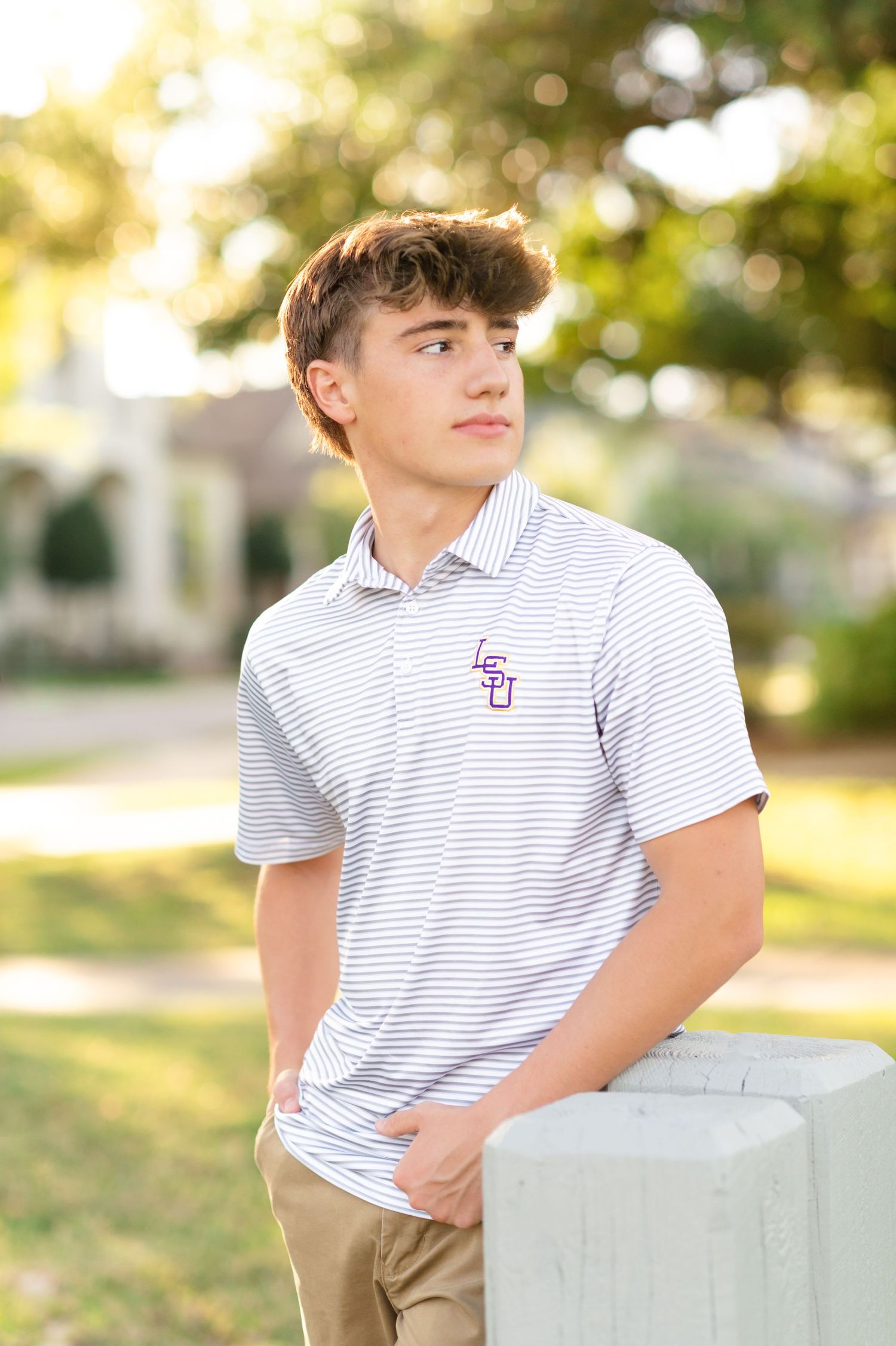 Young man in LSU striped polo shirt posing outdoors with bokeh green background in golden hour light.