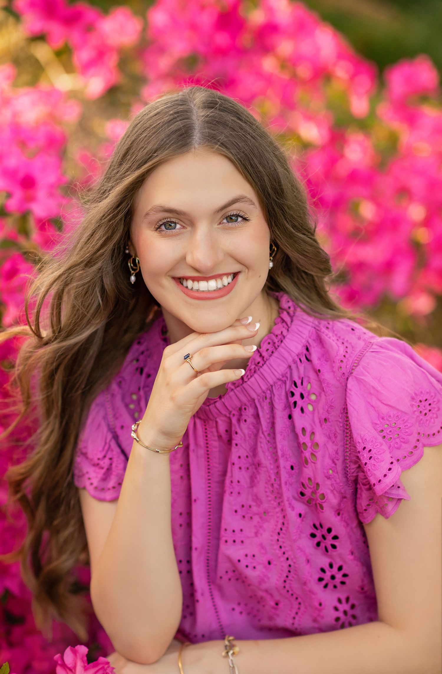 Young woman in purple eyelet top smiling outdoors with vibrant pink azalea flowers in the background.