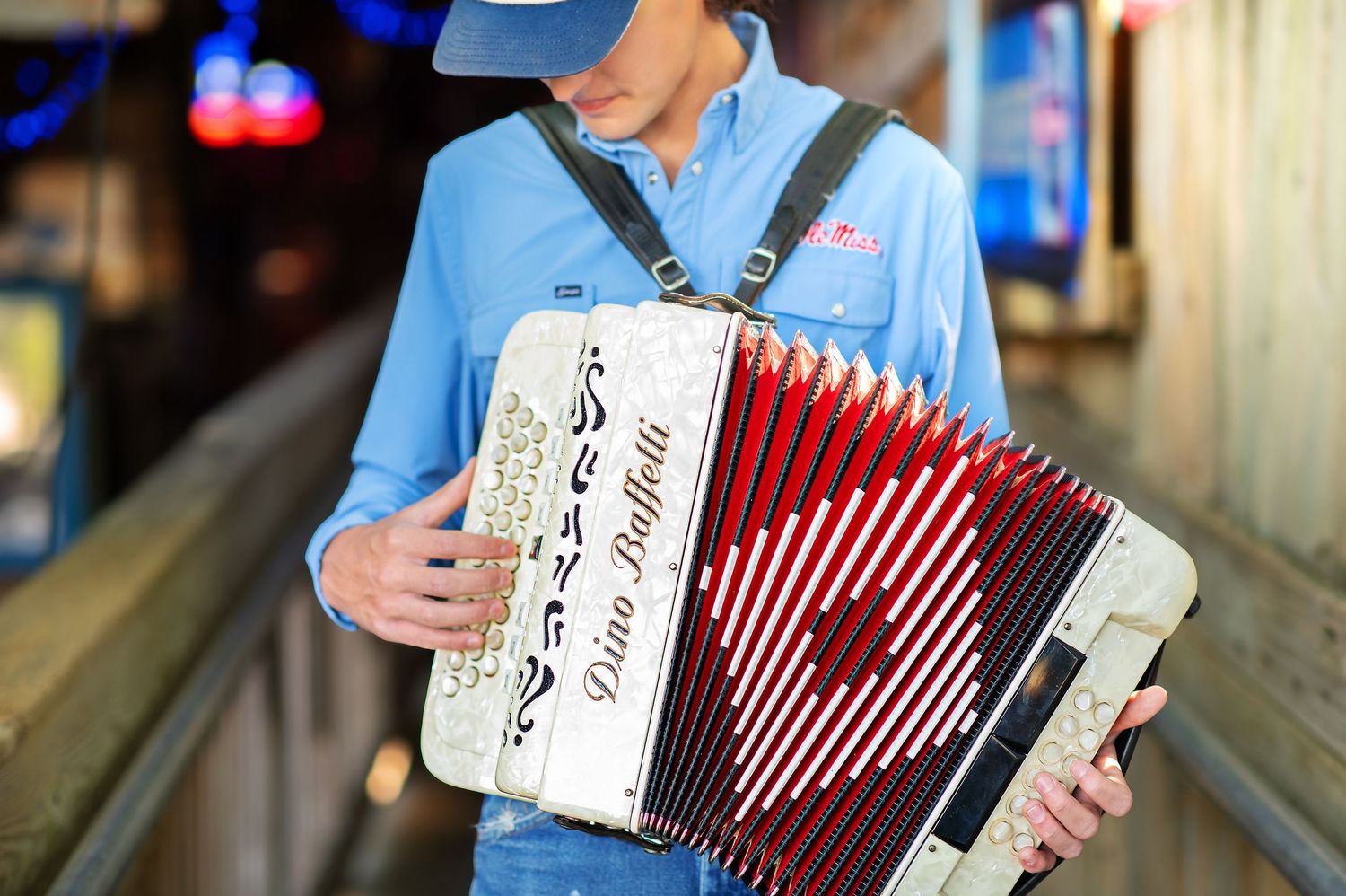 Man in blue shirt and cap playing a Dino Baffetti accordion outdoors.