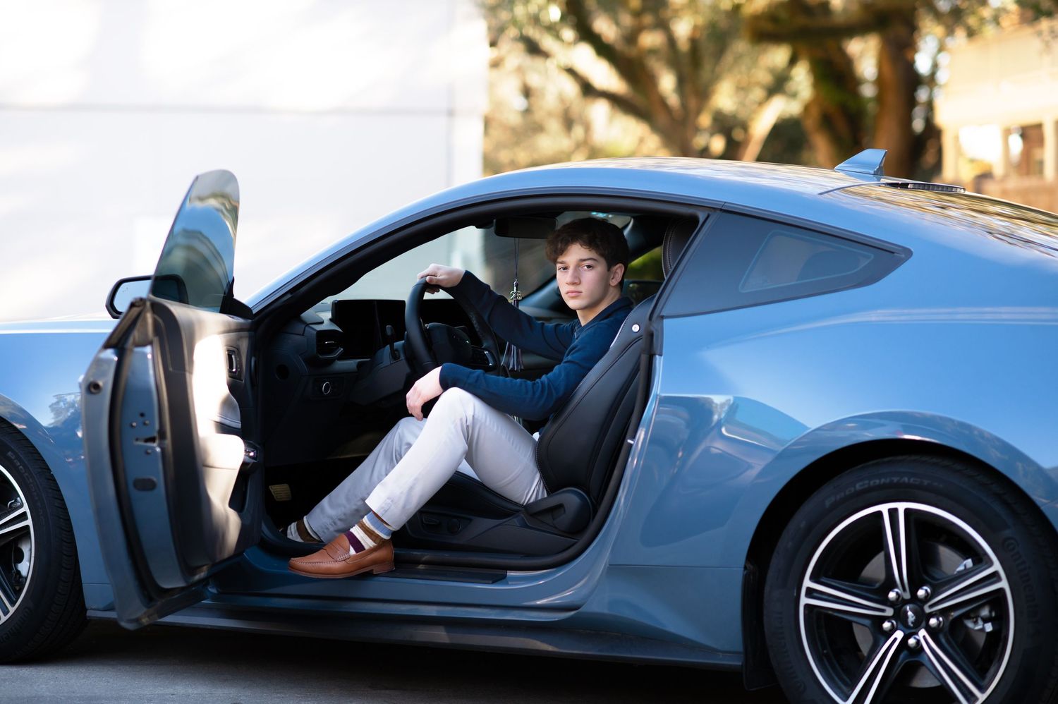 Young woman sitting in driver seat of a sleek blue sports coupe with door open, wearing casual attire.