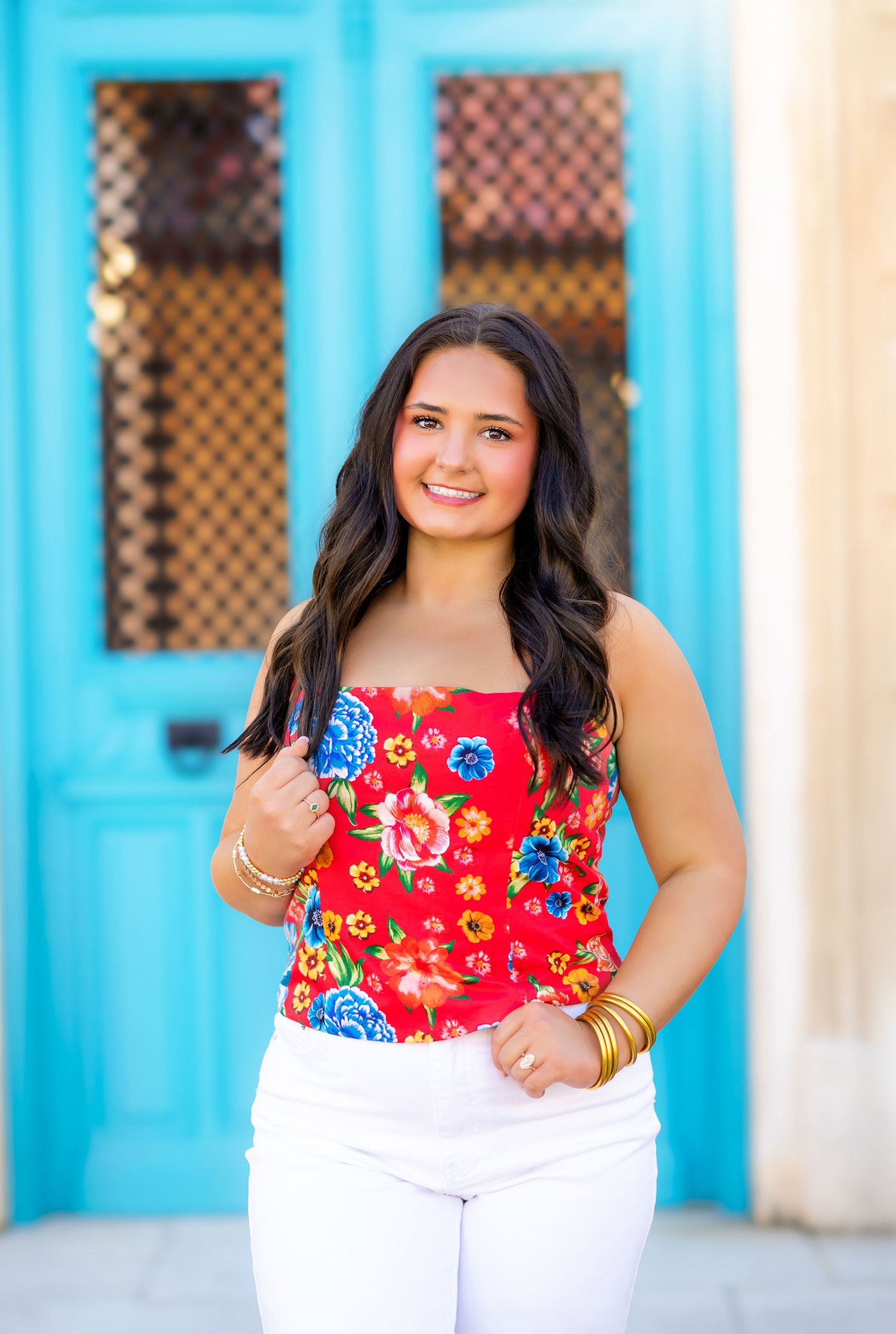 Smiling teen girl in red floral strapless top and white jeans poses before vibrant turquoise door.